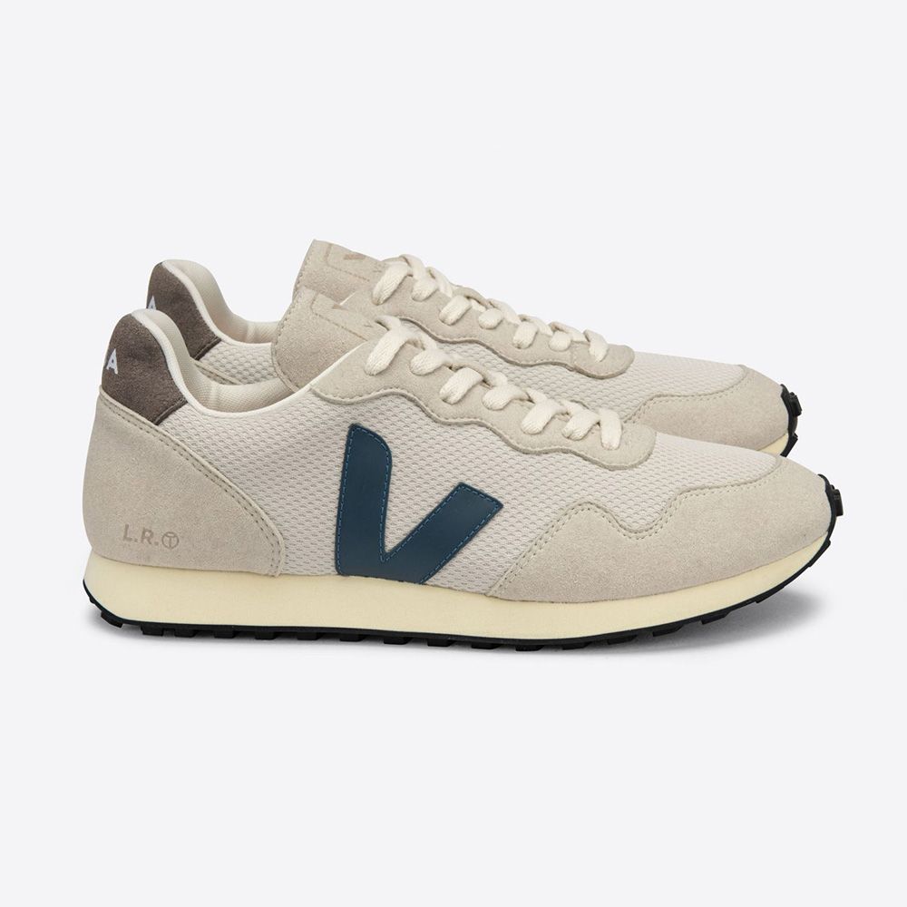 Ein Paar beigefarbene Sneaker mit dunkelblauem "V"-Logo und schwarzer Sohle auf weißem Hintergrund.