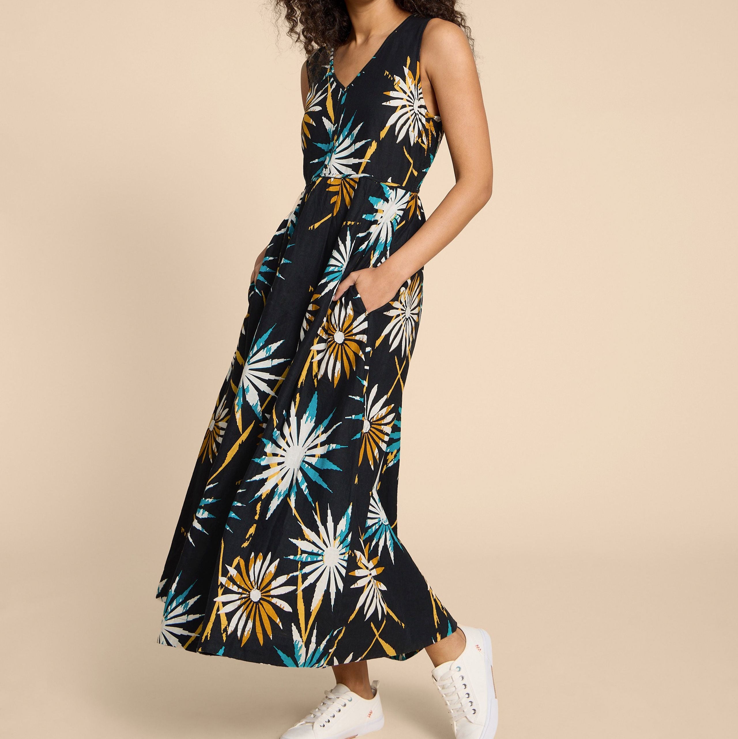 Frau in einem langen, schwarz gemusterten Sommerkleid mit Blumenmuster und weißen Sneakers.