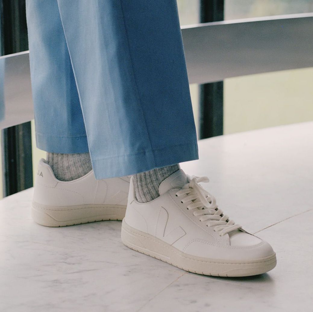 Person trägt weiße Turnschuhe und graue Socken zu einer hellblauen Hose, stehend auf einem hellen Marmorboden.