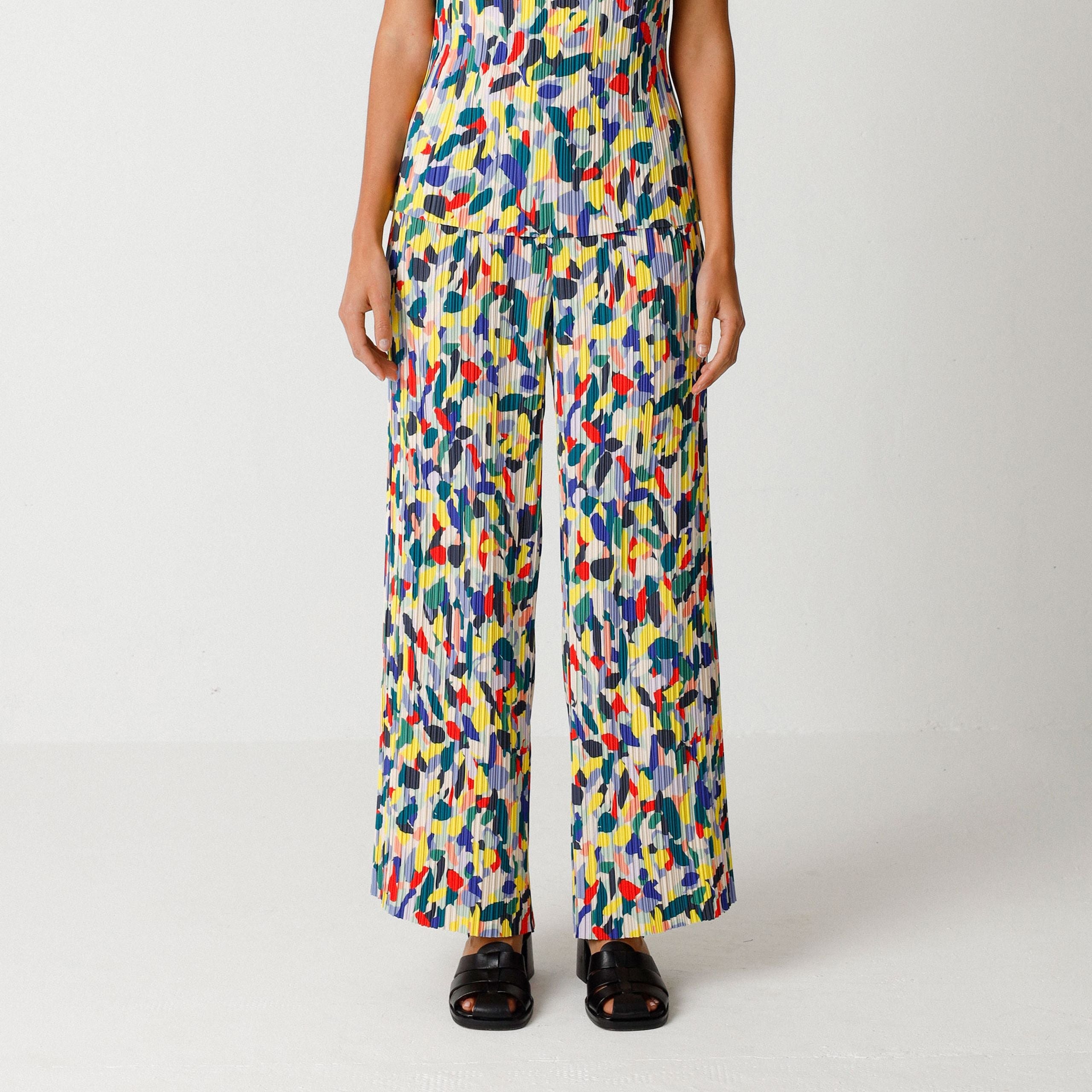 Frau trägt ein buntes, gemustertes Outfit mit weit geschnittener Hose und Top vor weißem Hintergrund.