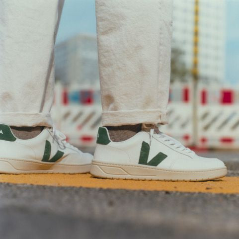 Person wearing weißes Sneakers mit grünem Logo und hochgekrempelten Jeans, steht auf der Straße, Hintergrund unscharf.