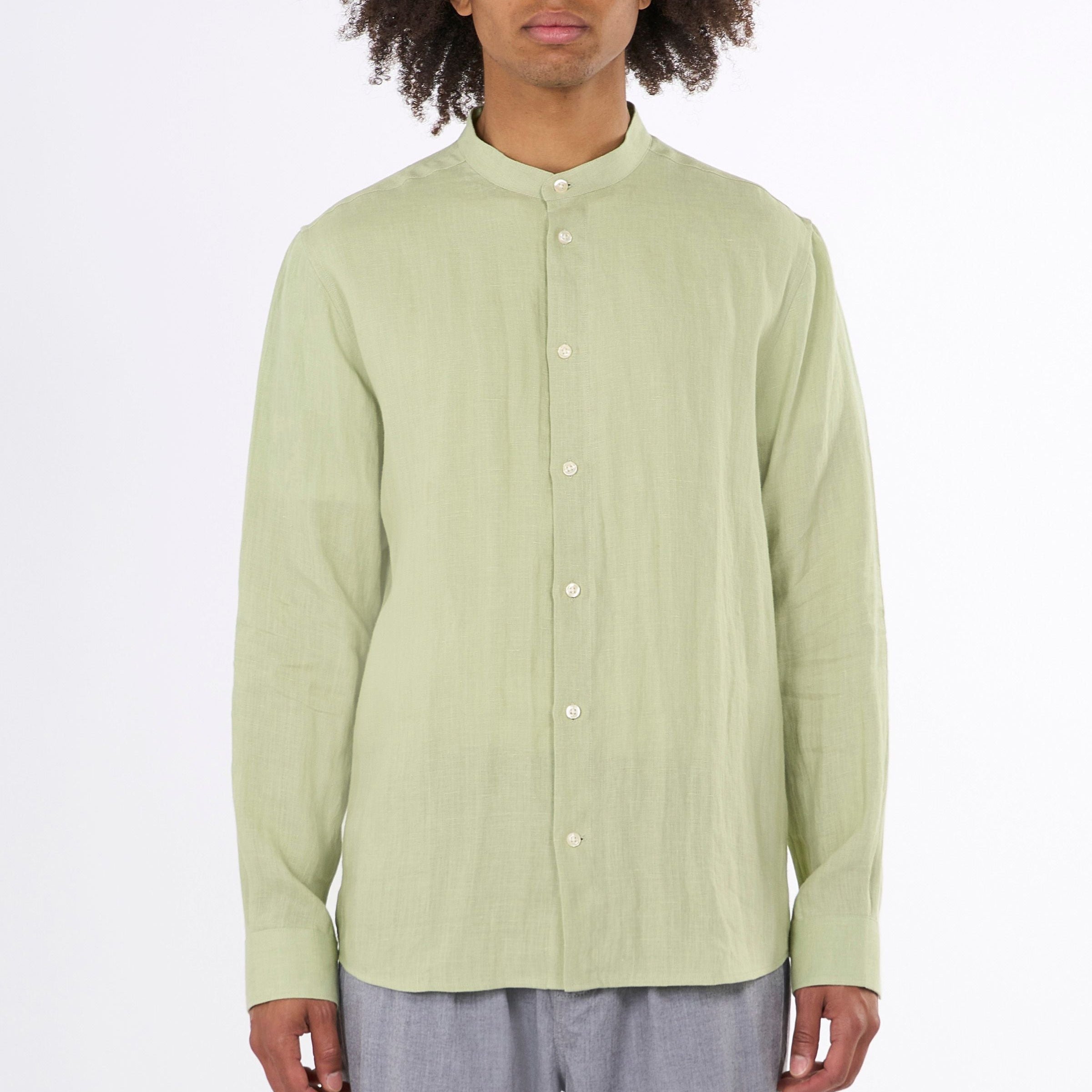 Mann trägt ein hellgrünes Hemd mit Stehkragen und grauer Hose vor weißem Hintergrund.