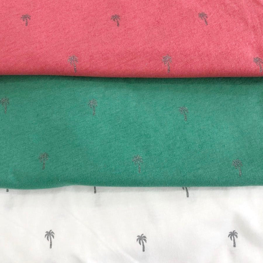 Drei Stoffstücke in Rot, Grün und Weiß mit kleinen Palmenmustern übereinander gestapelt.