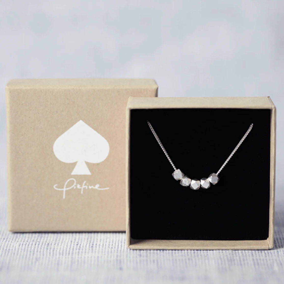 Schlichte Halskette mit facettierten Perlen in einer Geschenkbox mit Spadesymbol auf dem Deckel.