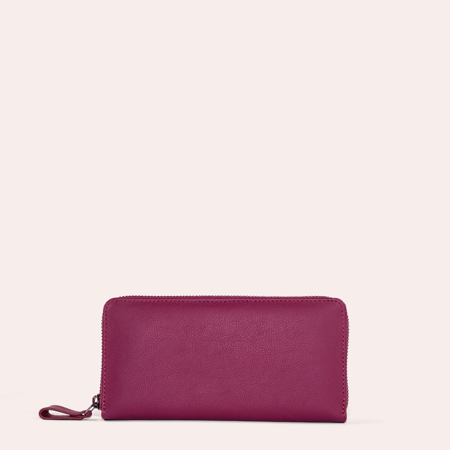 Eine magentafarbene Brieftasche mit Reißverschluss und Handschlaufe, die aufrecht vor einem hellbeigen Hintergrund steht.