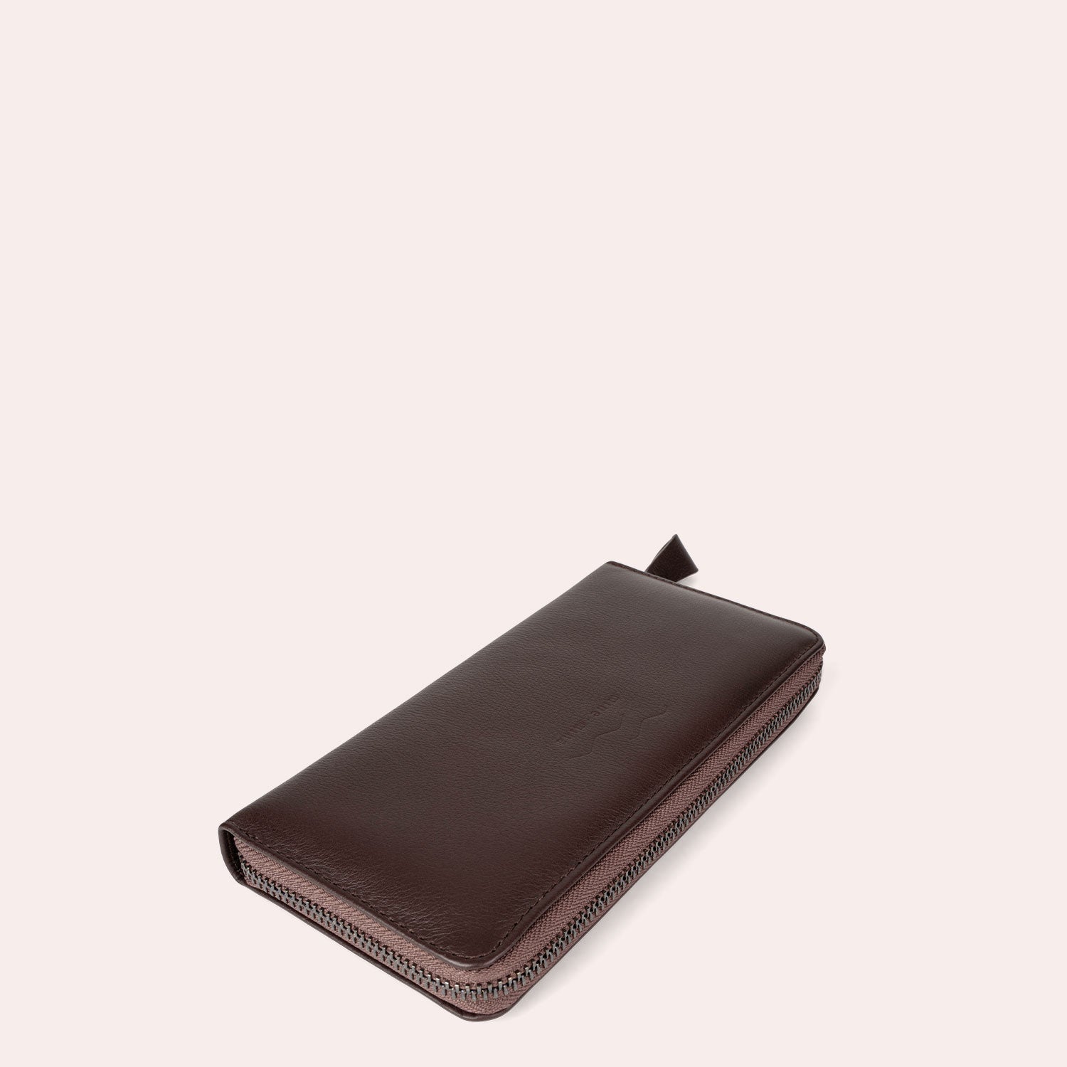 Ein braunes Lederportemonnaie mit Reißverschluss wird vor einem schlichten, hellen Hintergrund gezeigt, der seine glatte Textur und eine kleine Lederlasche am Reißverschluss zeigt.