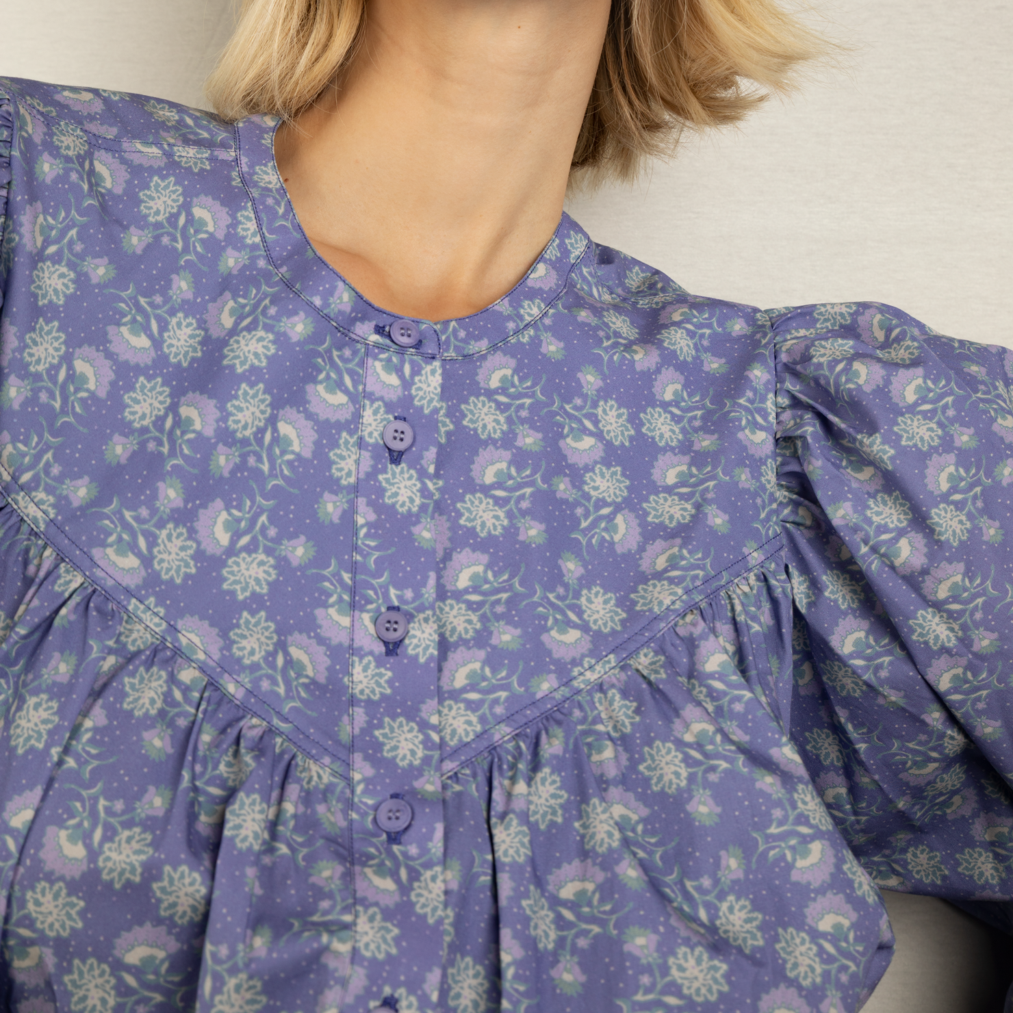Frau in lila Kleid mit Blumenmuster und Knopfdetails, Kopf nicht sichtbar.