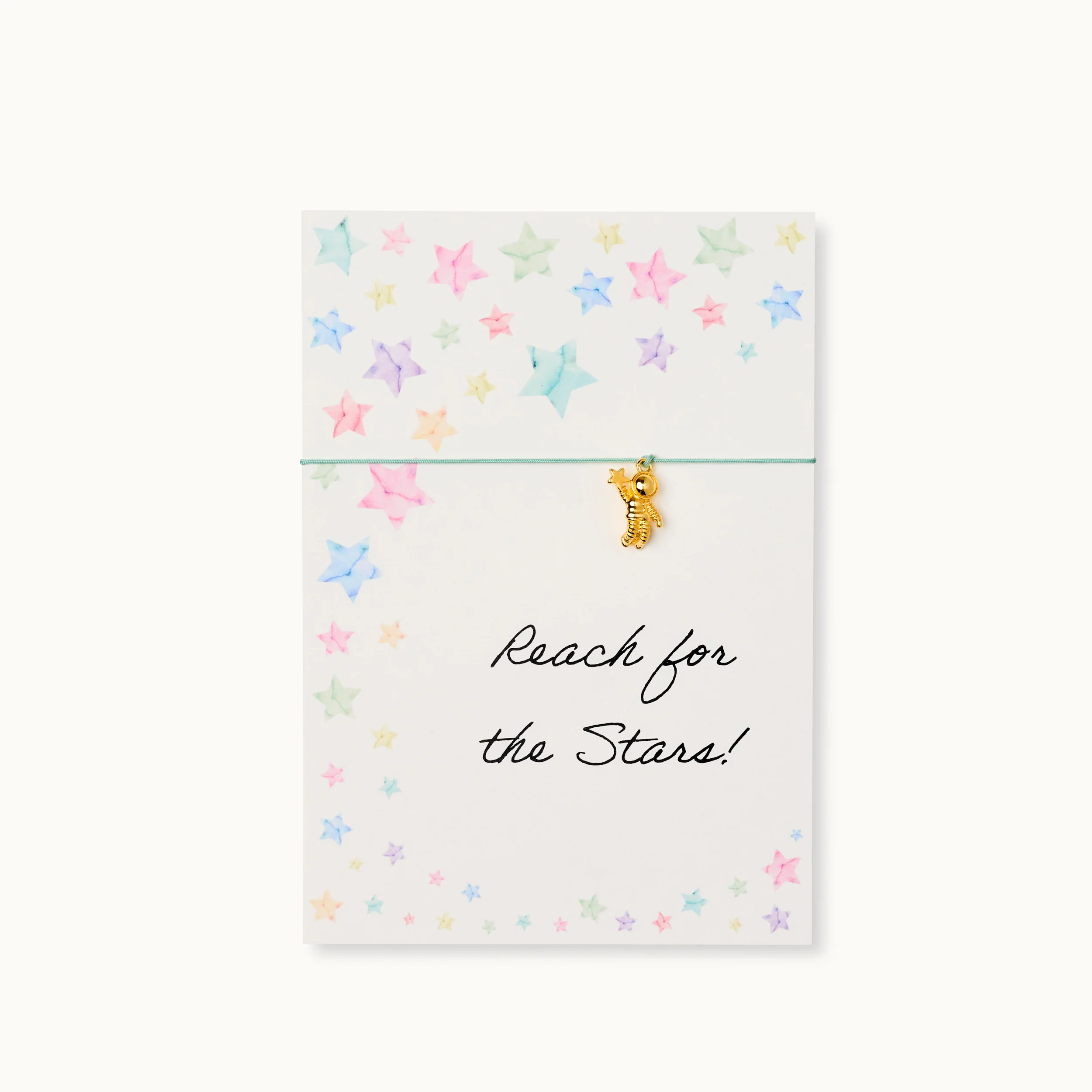 Weiße Karte mit bunten Sternen, grüner Schnur und einem goldenen Anhänger; Text: "Reach for the Stars!".