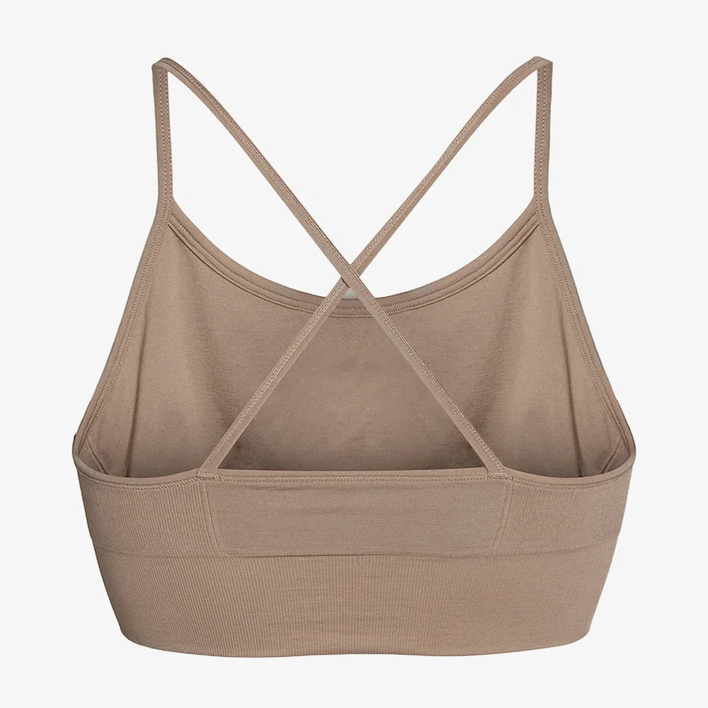 Ein taupefarbener, nahtloser Bralette mit dünnen, sich kreuzenden Trägern im Rücken und einem breiten, stützenden Band im unteren Bereich, der auf weißem Hintergrund zu sehen ist.