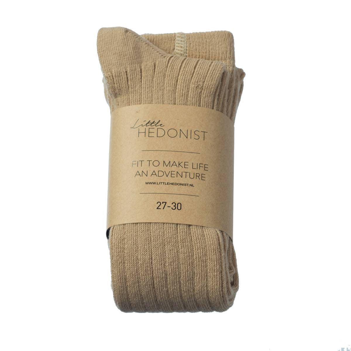 Ein Paar beigefarbene, gerippte Socken, zusammengefaltet und mit einem braunen Papieretikett umwickelt, auf dem steht: Little Hedonist, Fit to make life an adventure, 27-30.