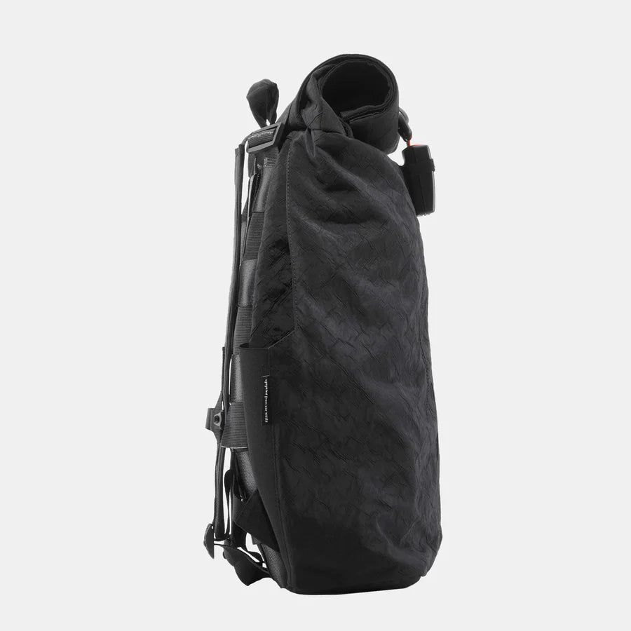 Schwarzer, seitlich aufgenommener Rucksack mit Rolltop-Verschluss und schlankem Design vor grauem Hintergrund.
