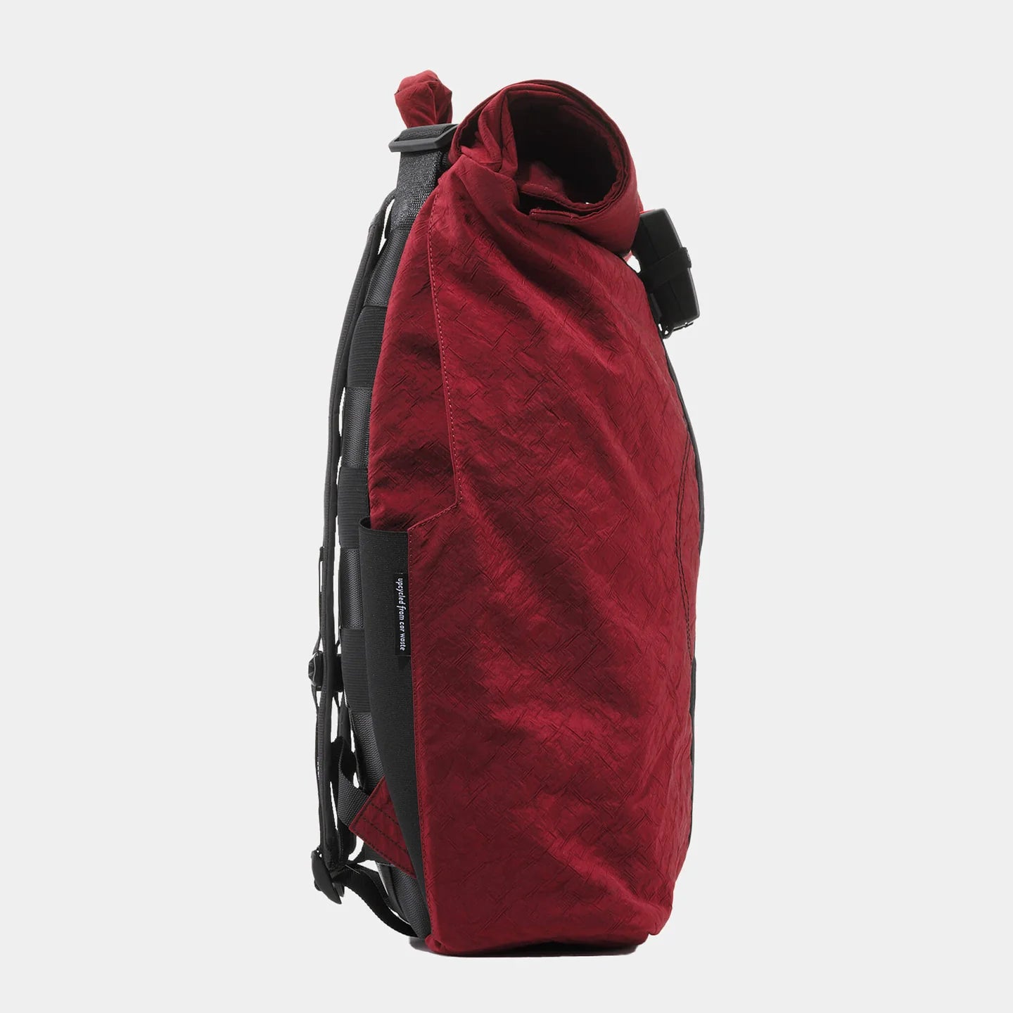 Ein roter Rucksack mit Rolltop-Verschluss, von der Seite fotografiert, auf weißem Hintergrund.