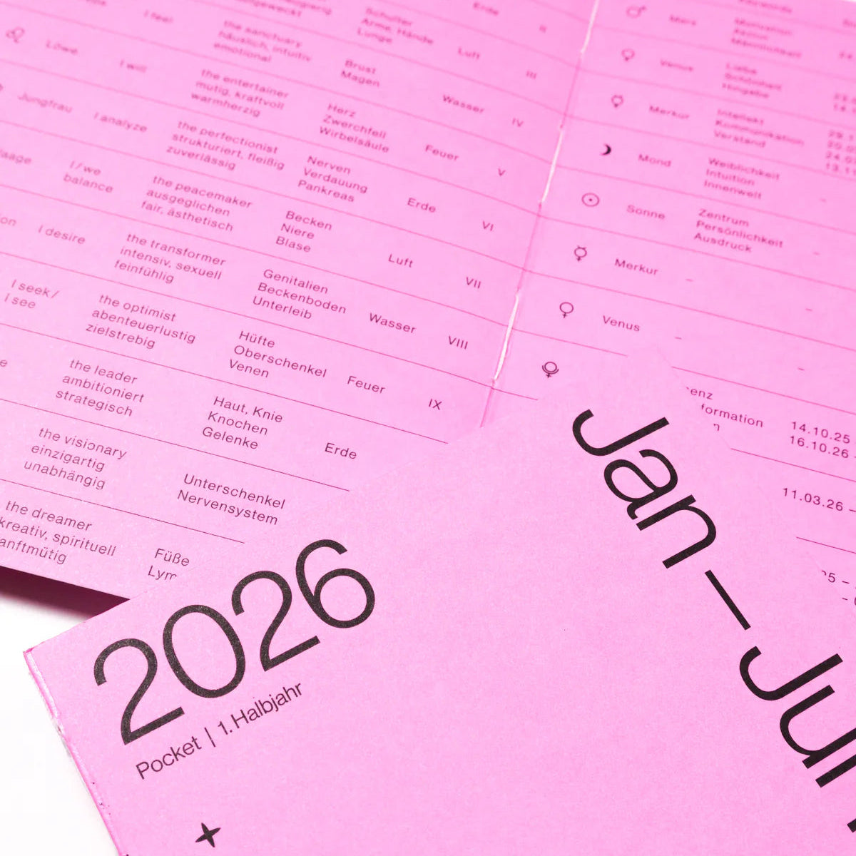 Ein rosafarbener Kalender für Januar bis Juli 2026 mit Datumsangaben, astrologischen Symbolen und Stichworten in deutscher Sprache, mit dem Aufdruck 2026 Pocket I. Halbjahr auf dem Umschlag.