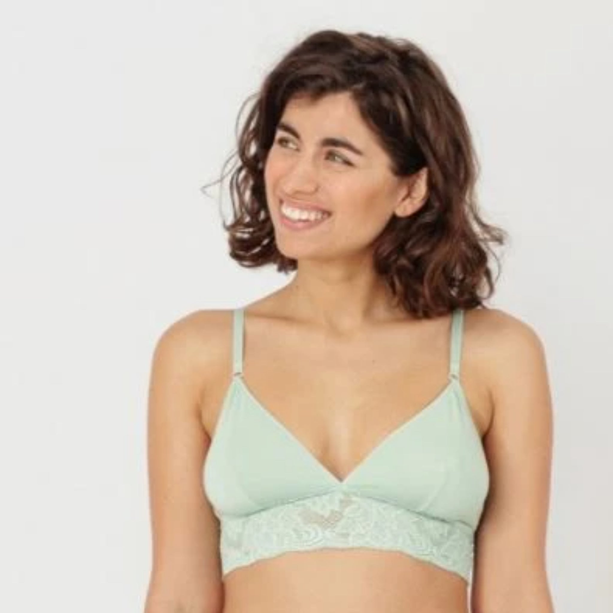 Eine Frau mit lockigem Haar trägt einen mintfarbenen Spitzen-BH und lächelt zur Seite.