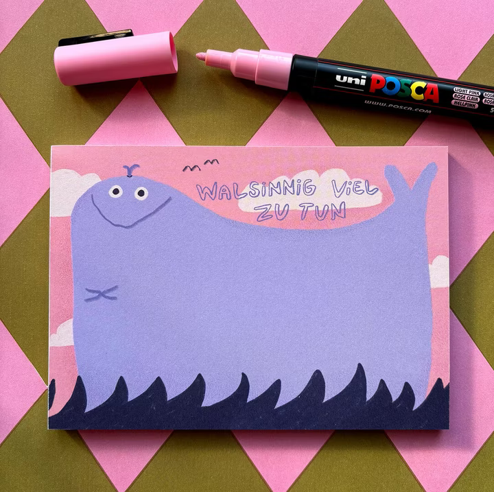 Eine Karte mit einem lila Wal und der Aufschrift "WALSINNIG VIEL ZU TUN" auf einem rosa Hintergrund mit einem pinken Stift.