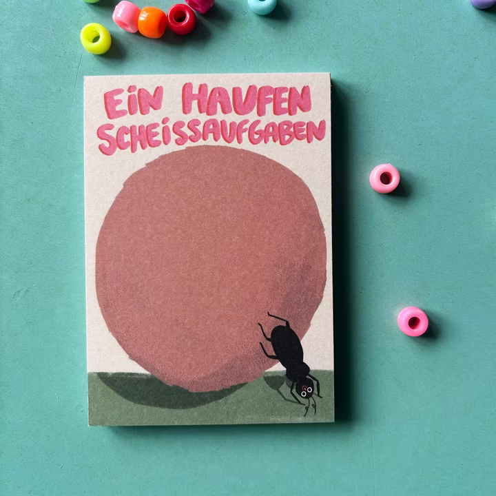 Postkarte mit Text "Ein Haufen Scheißaufgaben" und einem Mistkäfer, umgeben von bunten Perlen auf grünem Hintergrund.