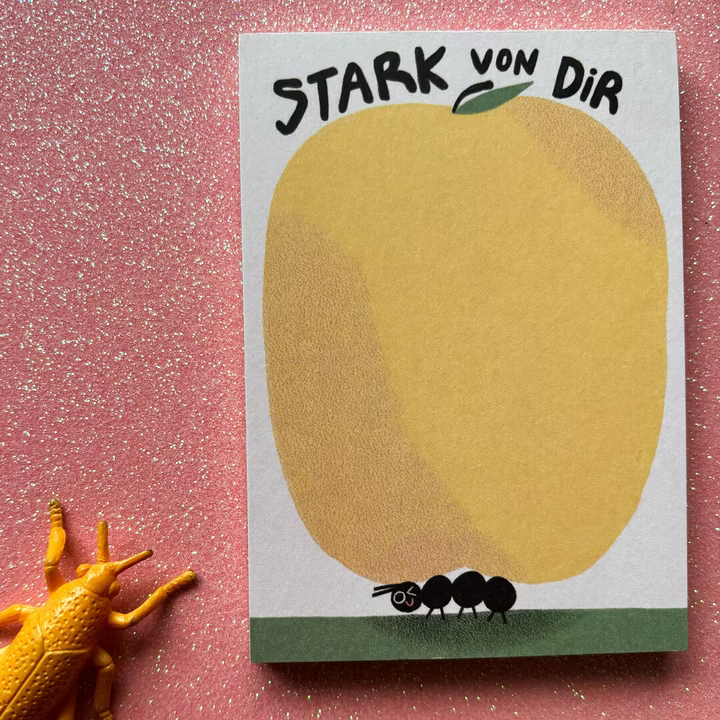 Eine Karte mit einem gelben Kreis und einer Ameise darunter auf glitzerndem pinken Hintergrund neben einem Spielzeugkäfer.