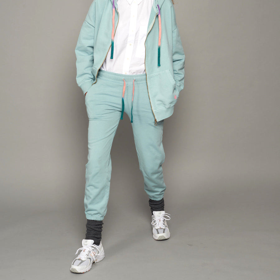 Person in mintgrünem Jogginganzug mit weißen Sneakers und grauen Socken auf grauem Hintergrund.