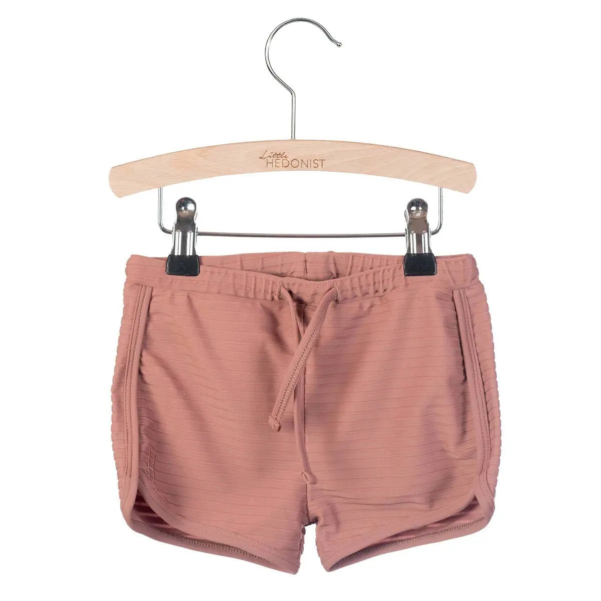 Hellrosa gerippte Shorts mit Kordelzug in der Taille, ausgestellt auf einem Holzbügel mit der Aufschrift Little HEDONIST, auf weißem Hintergrund.