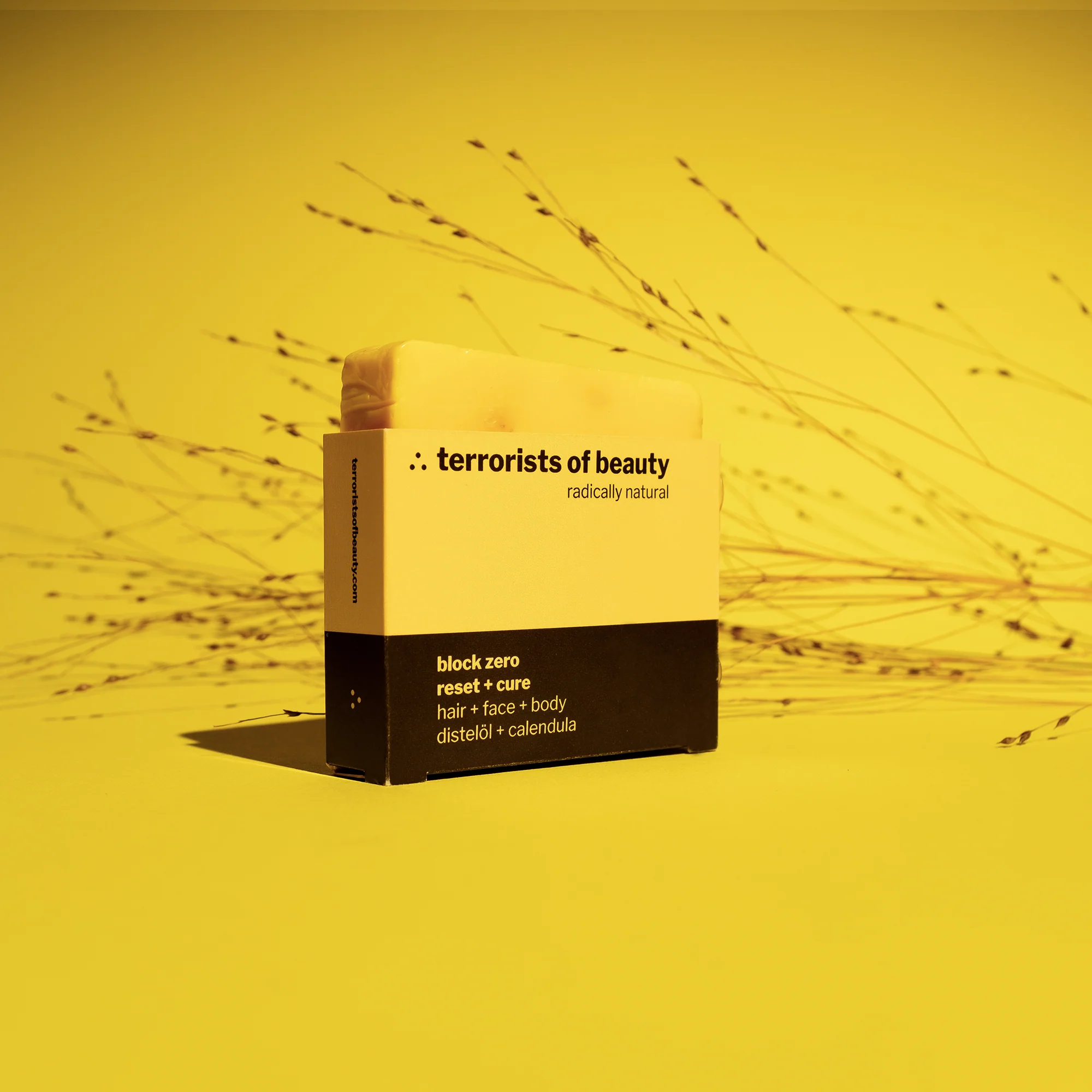 Gelbe Verpackung eines "terrorists of beauty"-Seifenprodukts, im Hintergrund getrocknete Gräser.