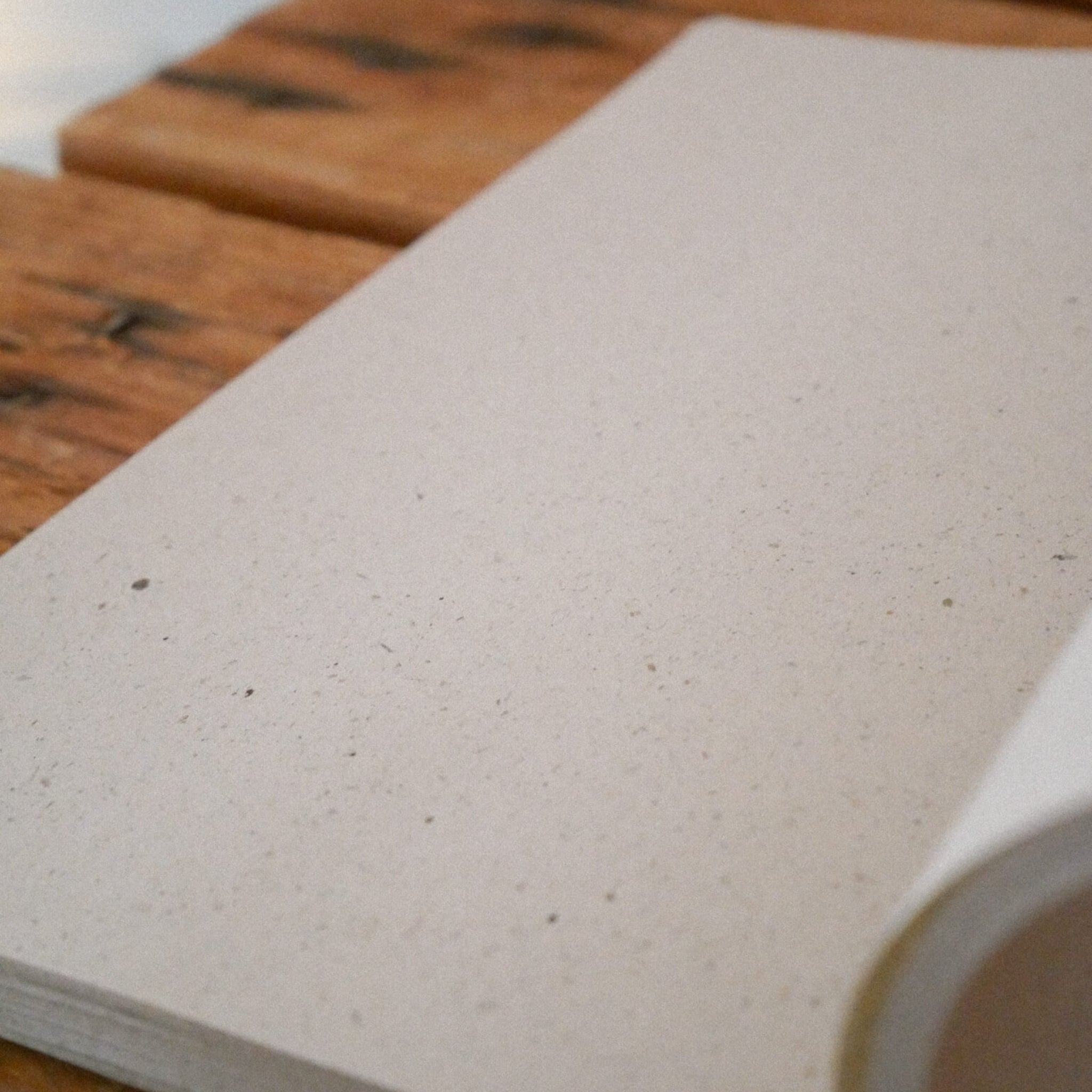 Ein aufgeschlagenes Notizbuch mit leeren, strukturierten Seiten liegt auf einer Holzoberfläche. Das Notizbuch ist angewinkelt, so dass die Wölbung der Seiten auf der rechten Seite zu sehen ist.