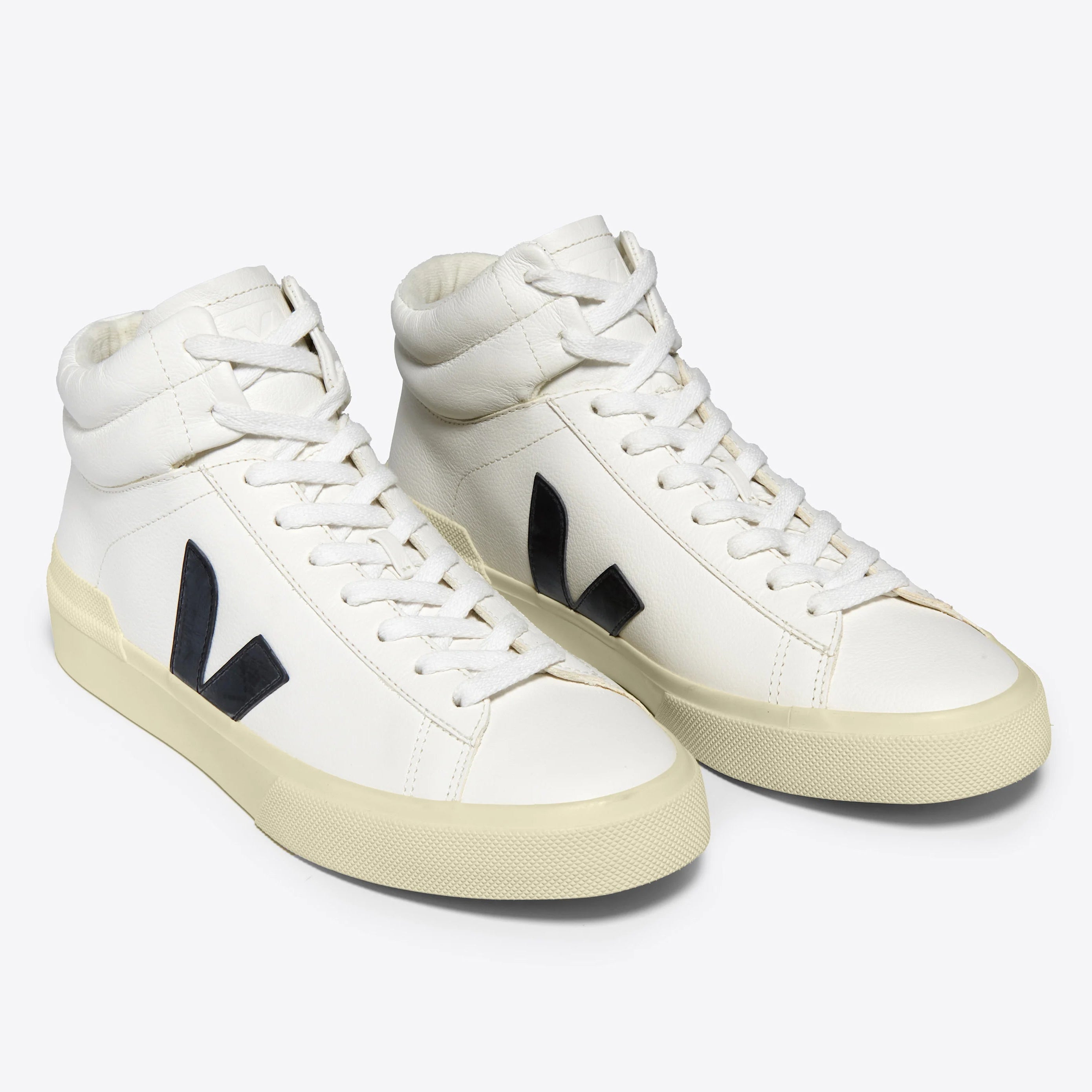 Ein Paar weiße High-Top-Sneakers mit beiger Sohle und schwarzem V-Logo an den Seiten auf einem einfarbigen hellgrauen Hintergrund.