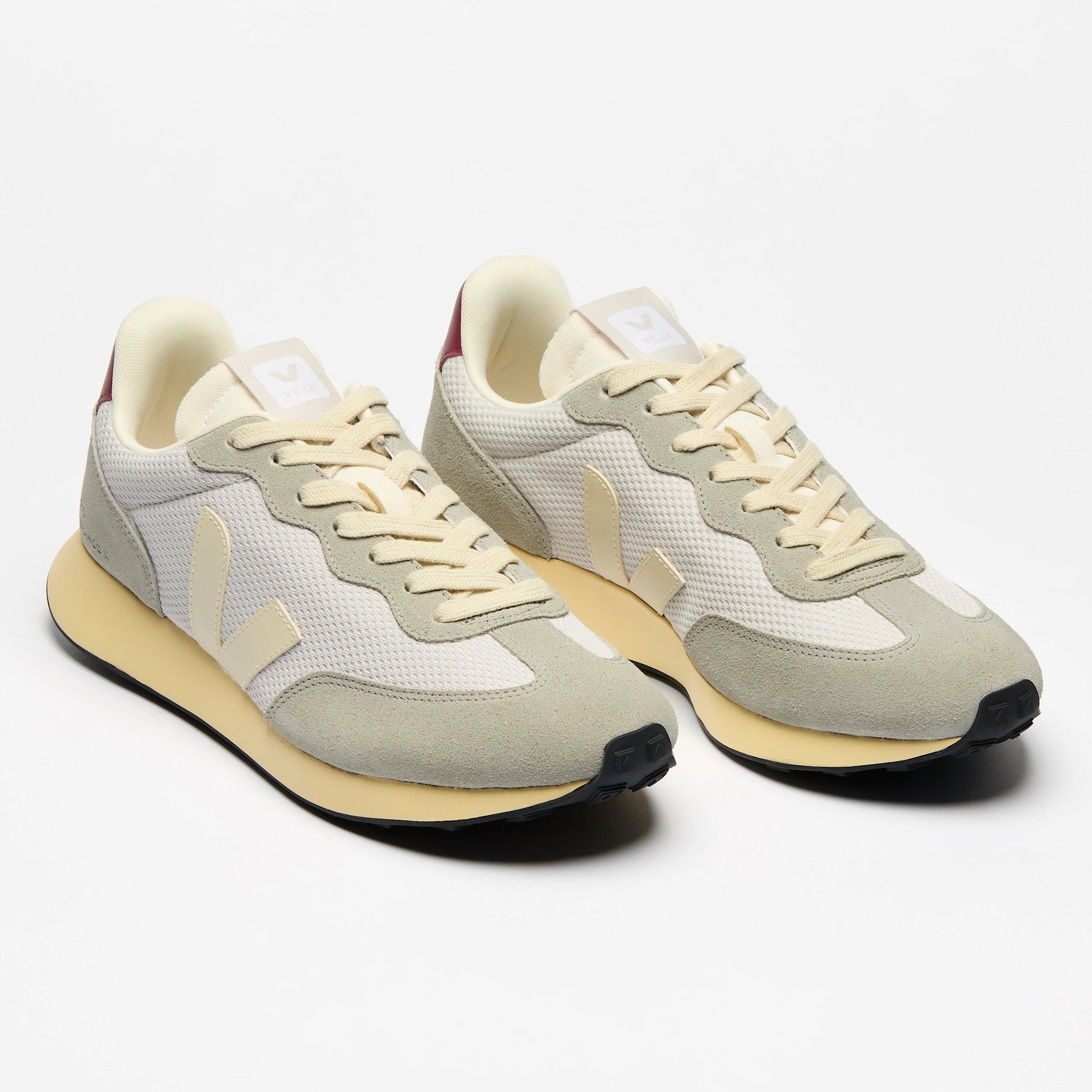 Ein Paar hellbeige-weiße Turnschuhe mit cremefarbenen Schnürsenkeln, beigen Sohlen und einem weißen V-Logo an den Seiten auf einem schlichten weißen Hintergrund.