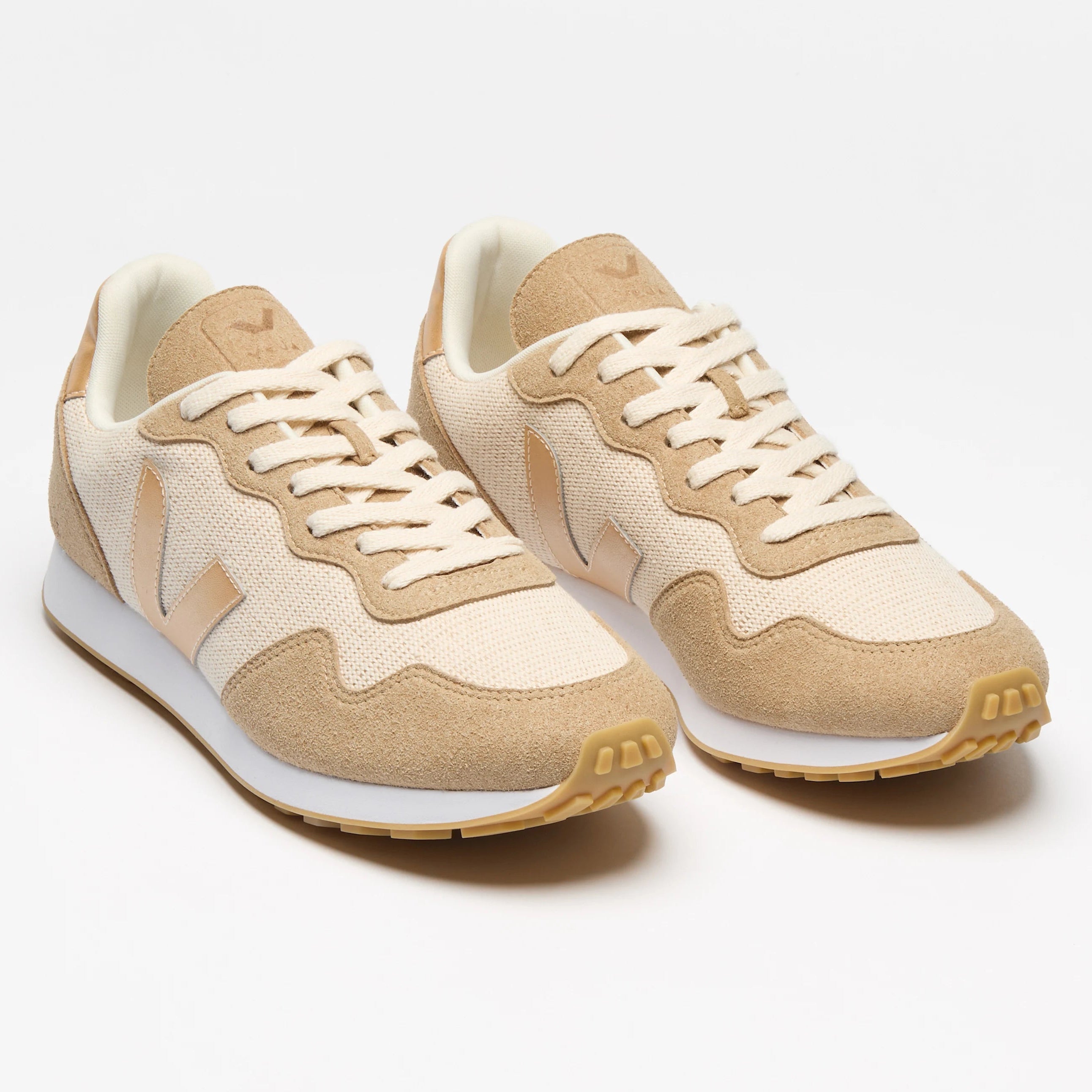 Ein Paar beigefarbene und weiße Sportschuhe mit weißen Schnürsenkeln und gummifarbenen Sohlen auf weißem Hintergrund.
