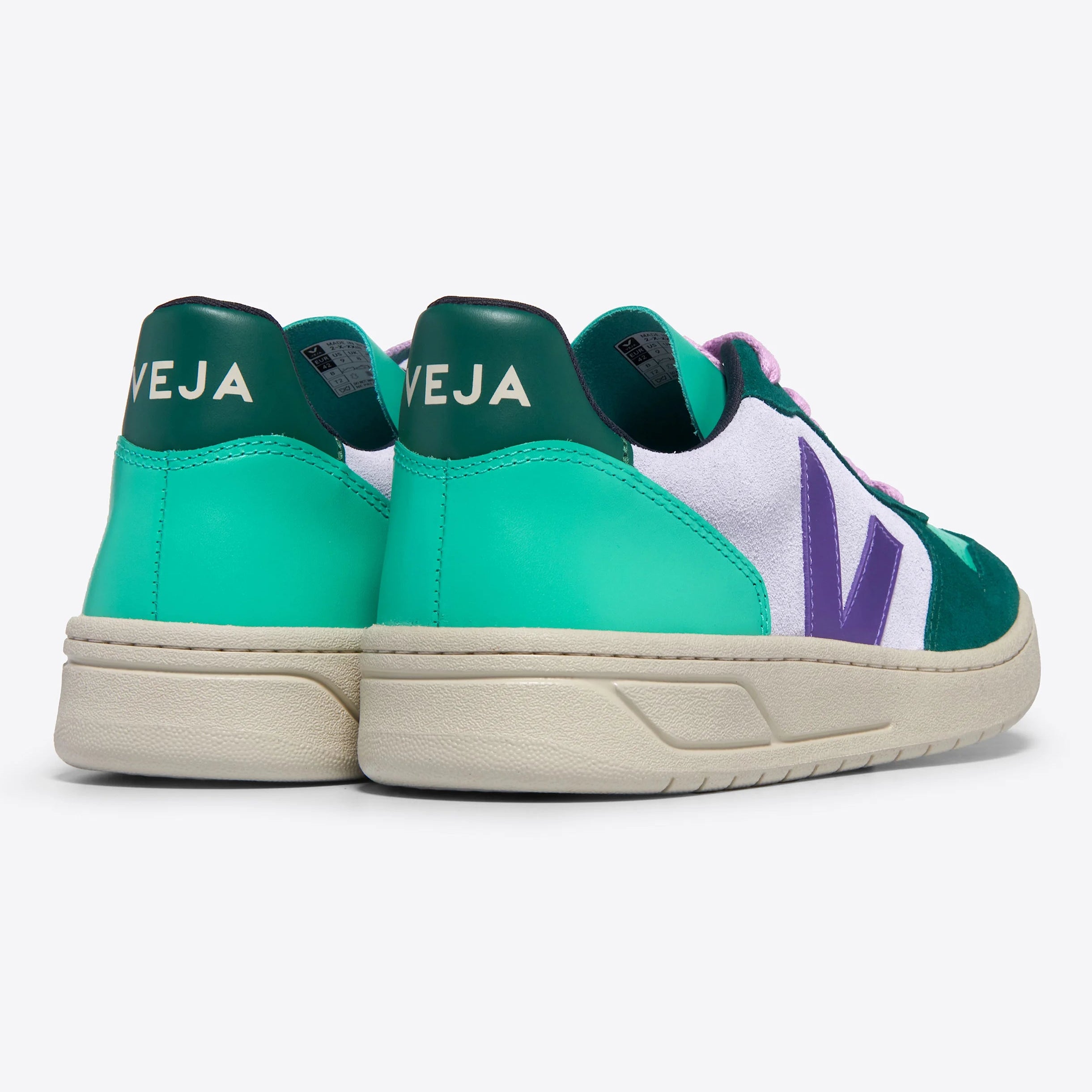 Ein Paar Veja-Turnschuhe mit grünen und blaugrünen Absätzen, weißen Seiten, lila V-Logos und cremefarbenen Sohlen, von hinten und von der Seite vor einem hellen Hintergrund betrachtet.
