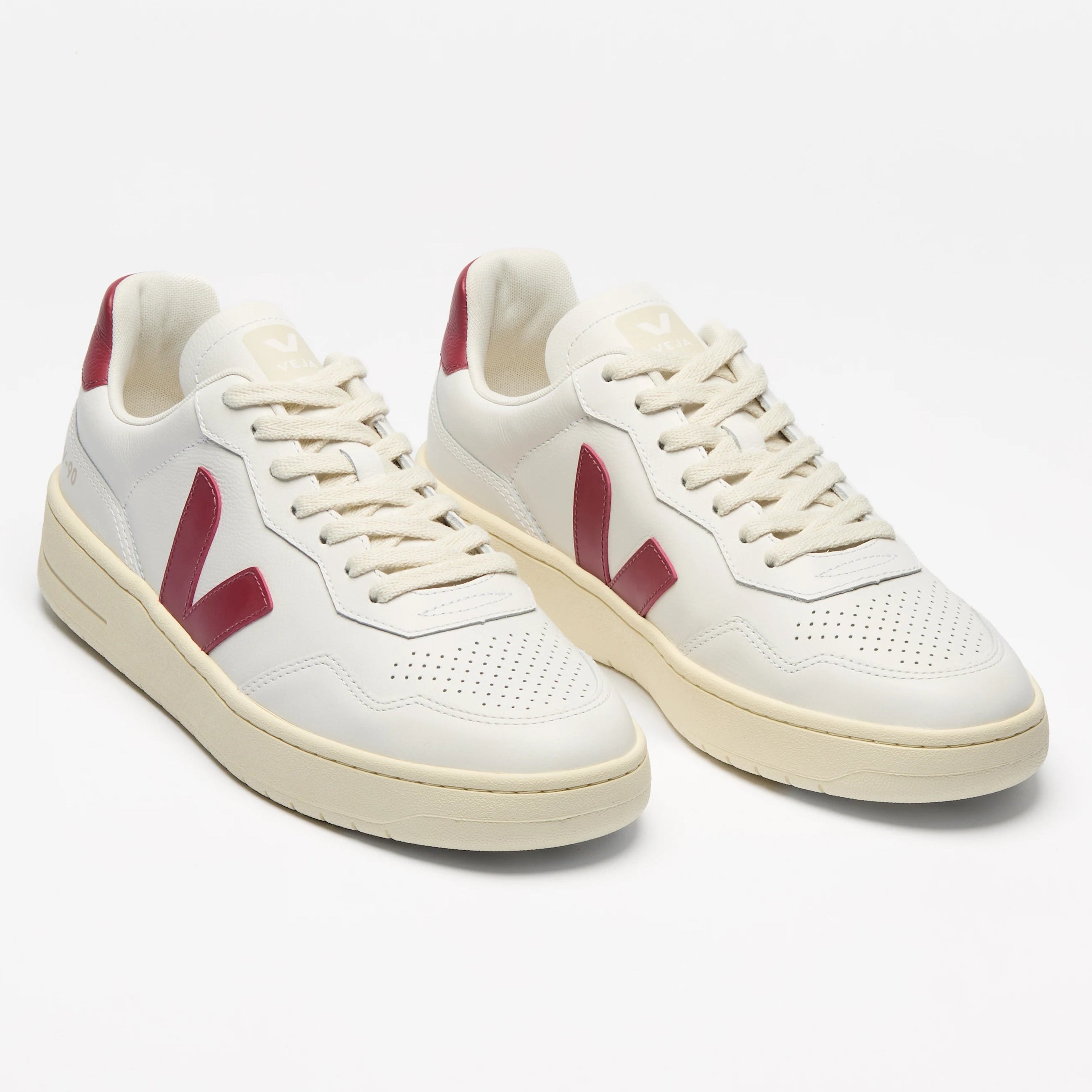 Ein Paar weißer Turnschuhe mit cremefarbener Sohle und rotem "V"-Logo an den Seiten auf weißem Hintergrund.