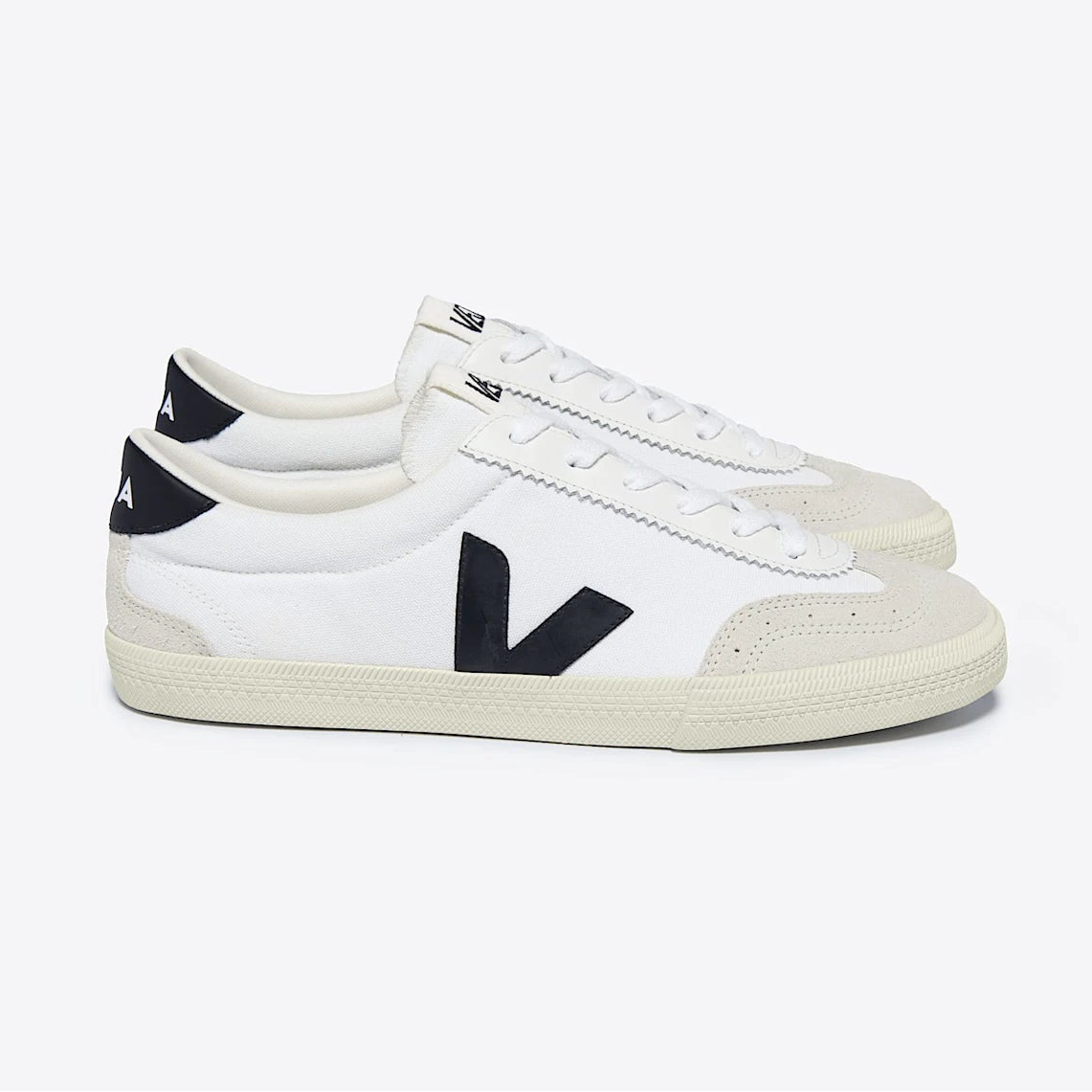 Ein Paar weiße Low-Top-Sneaker mit beiger Sohle und Zehenkappe, schwarzen V-förmigen Logos an den Seiten und schwarzen Fersenlaschen auf hellgrauem Hintergrund.