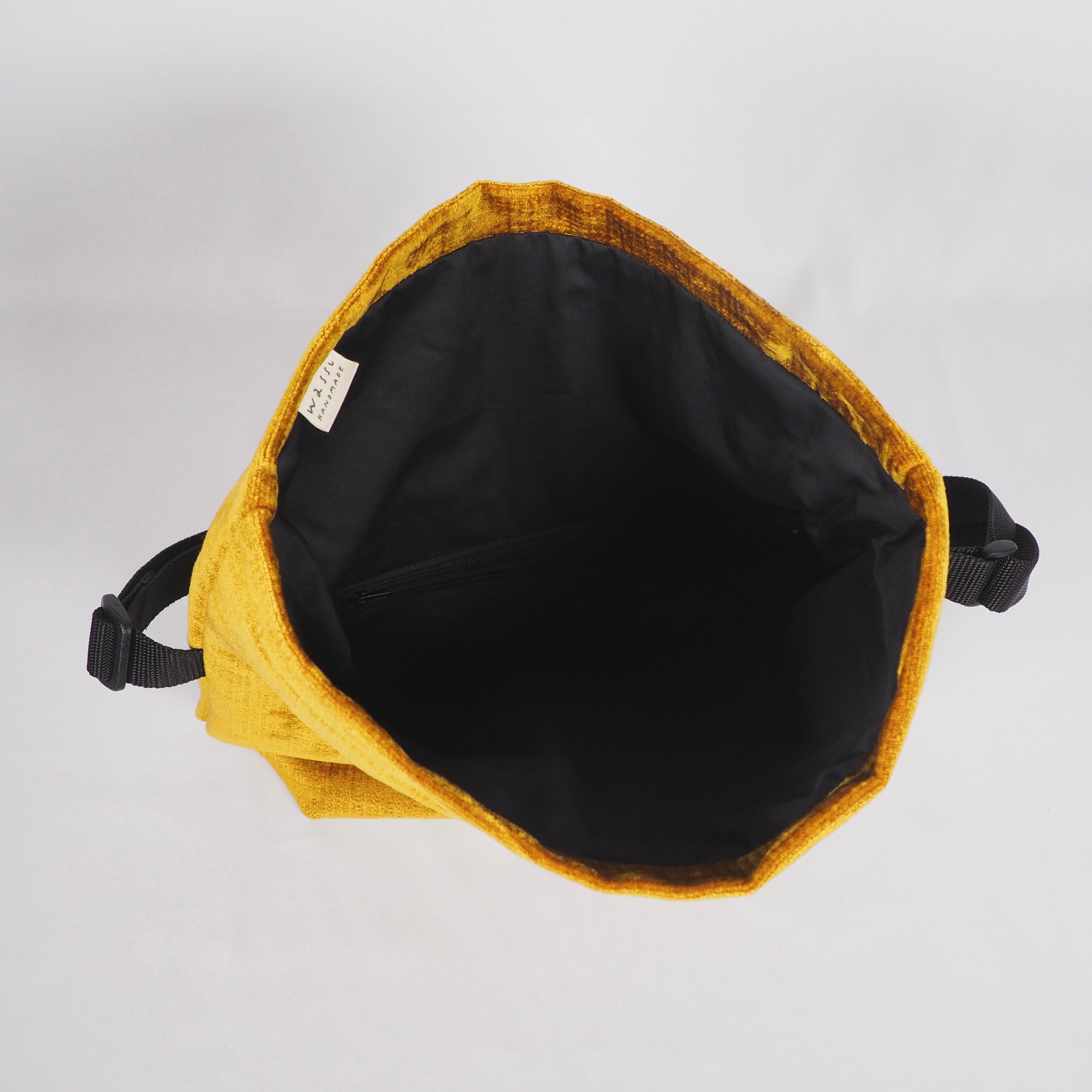 Gelbe Umhängetasche mit schwarzem Innenfutter und Reißverschluss, von oben fotografiert.