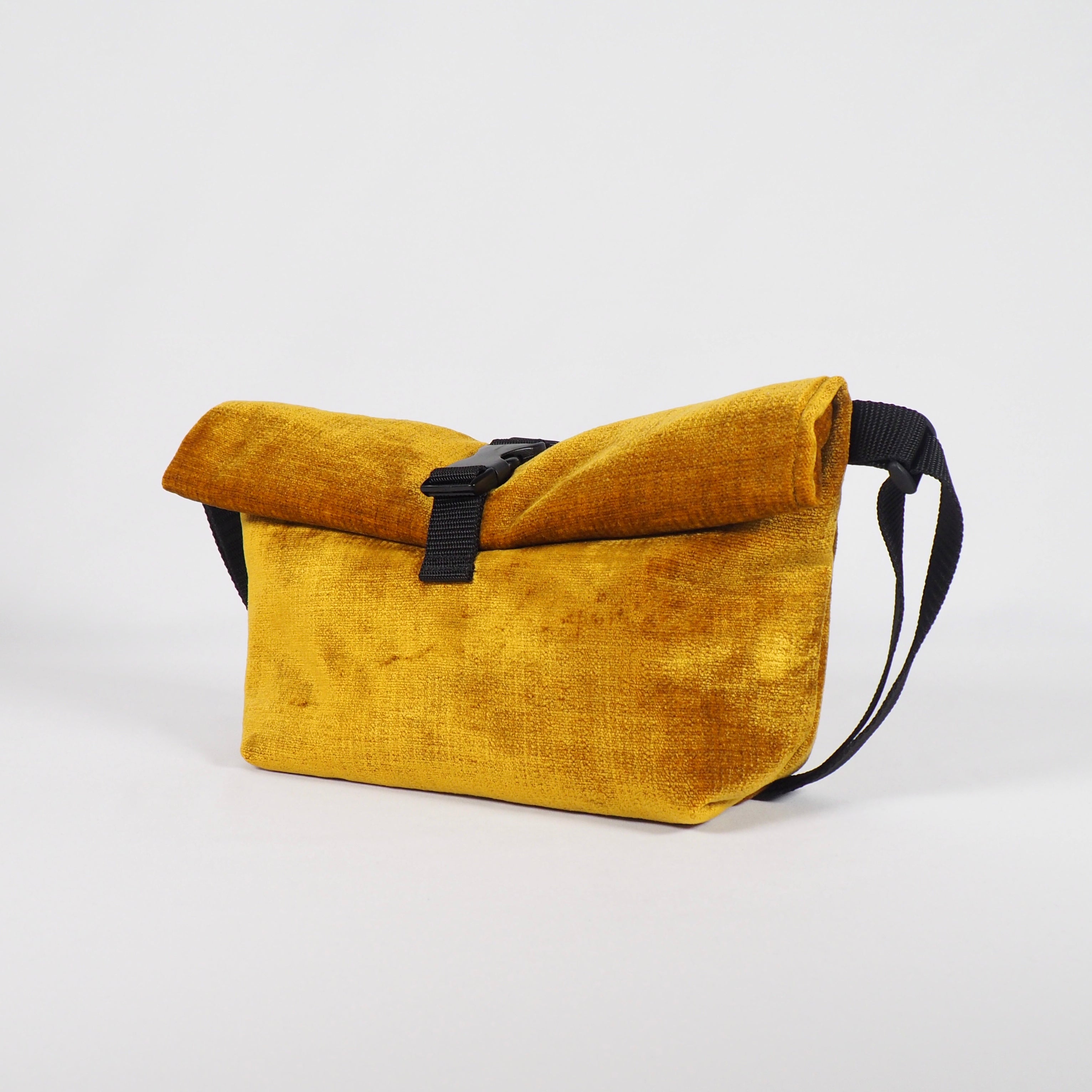 Gelbe Stofftasche mit schwarzem Schultergurt und Schnalle auf weißem Hintergrund.