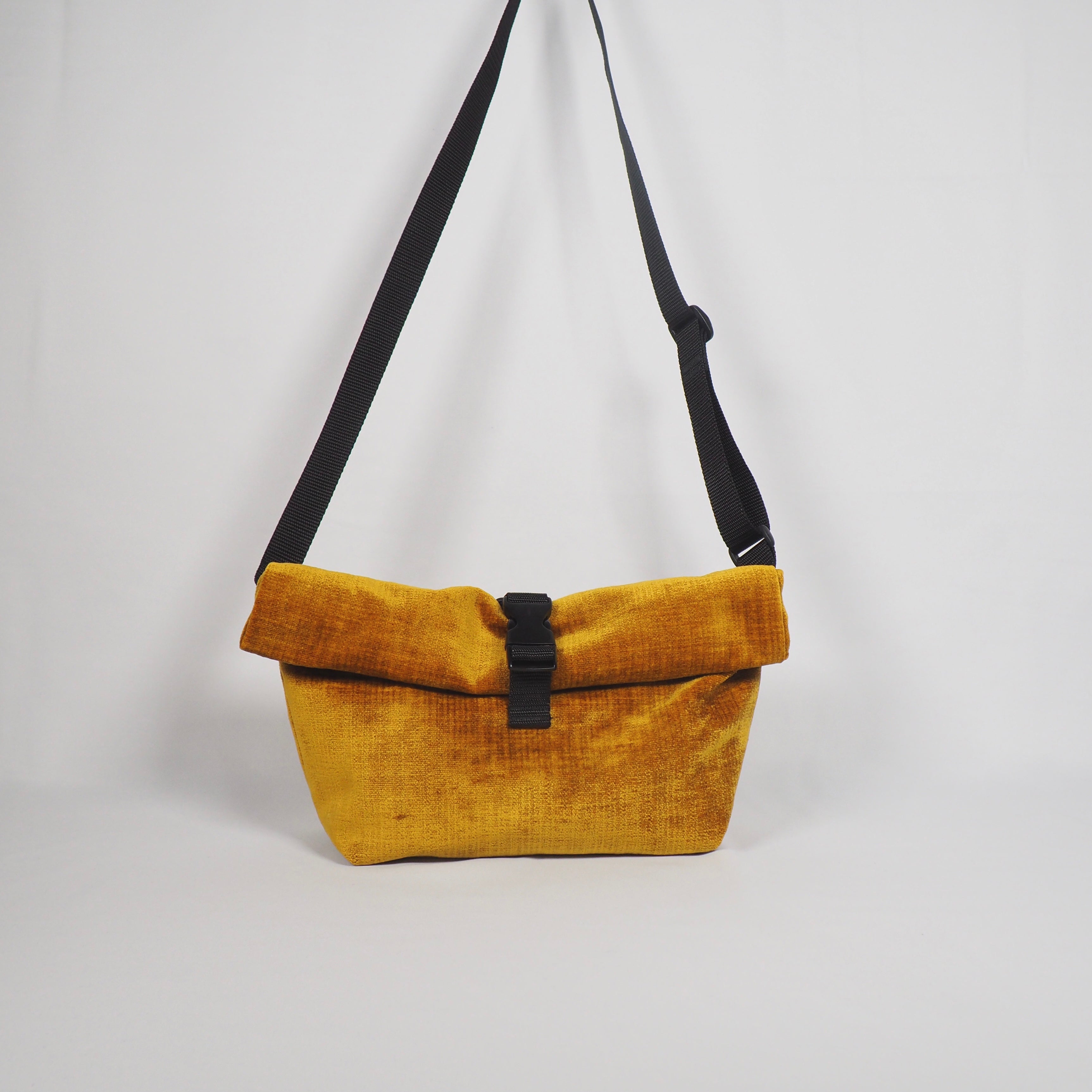Gelbe Umhängetasche mit schwarzem Riemen und Schnalle vor weißem Hintergrund.