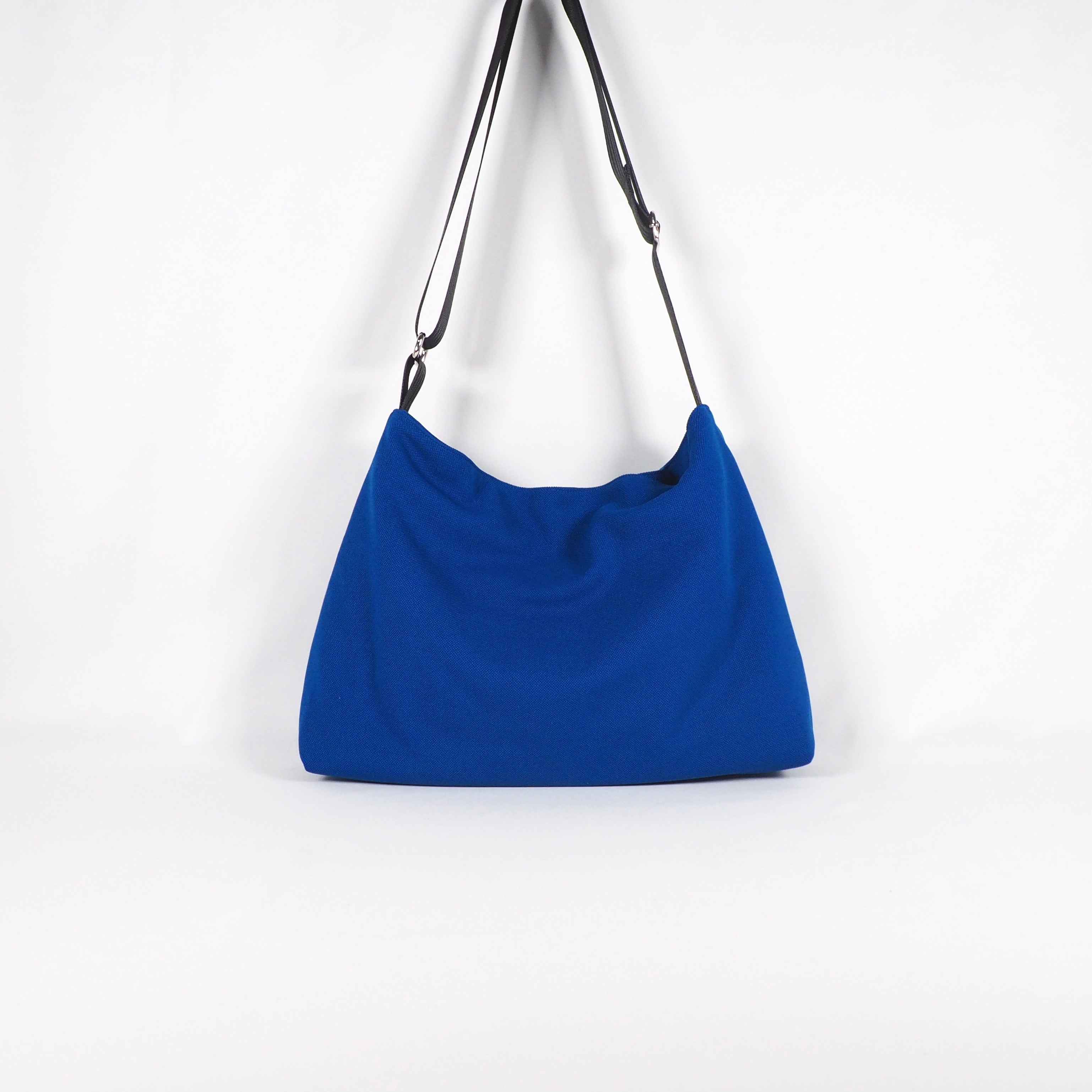 Blaue Handtasche mit schwarzem Schulterriemen auf weißem Hintergrund.