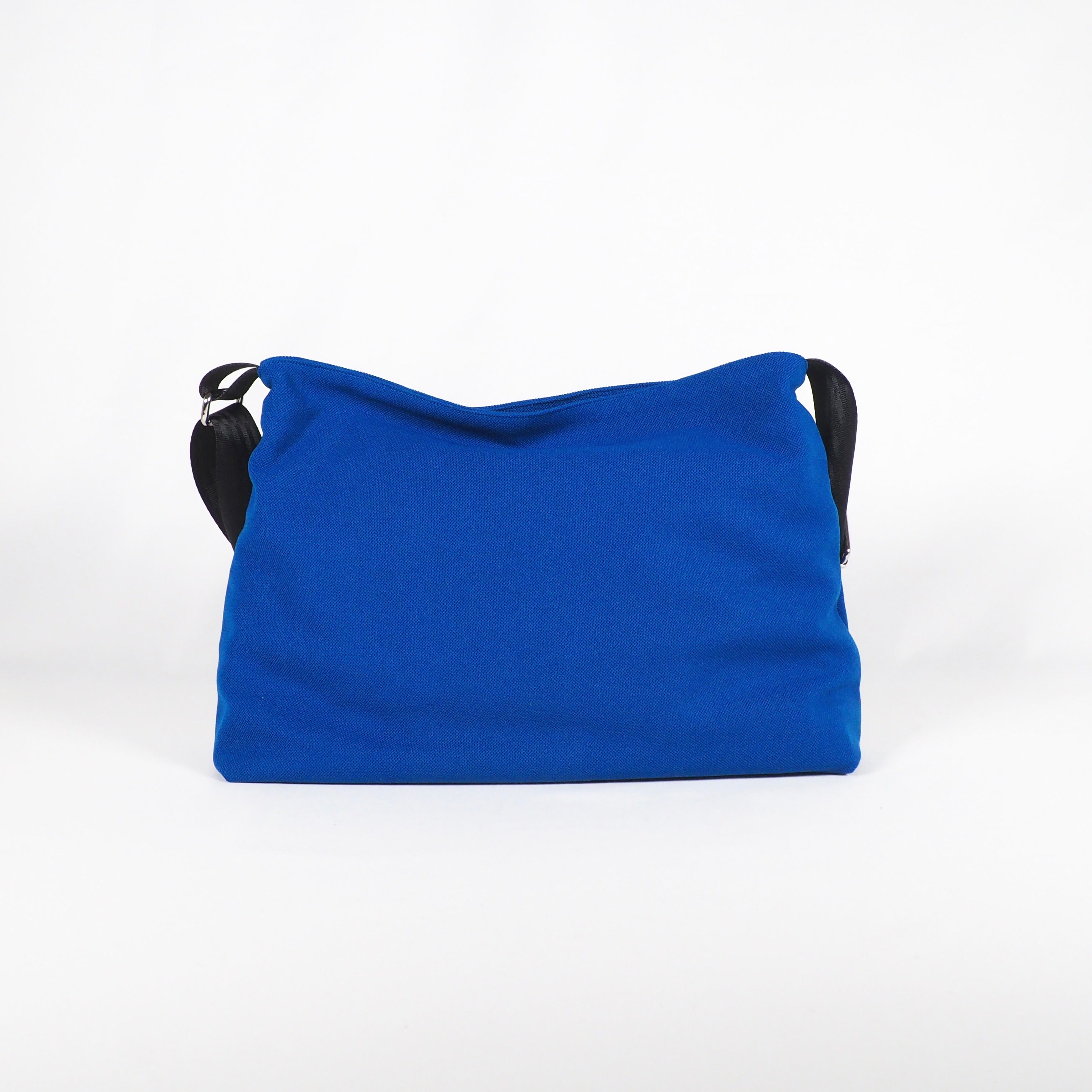 Blaue Stofftasche mit schwarzem Trageriemen vor weißem Hintergrund.