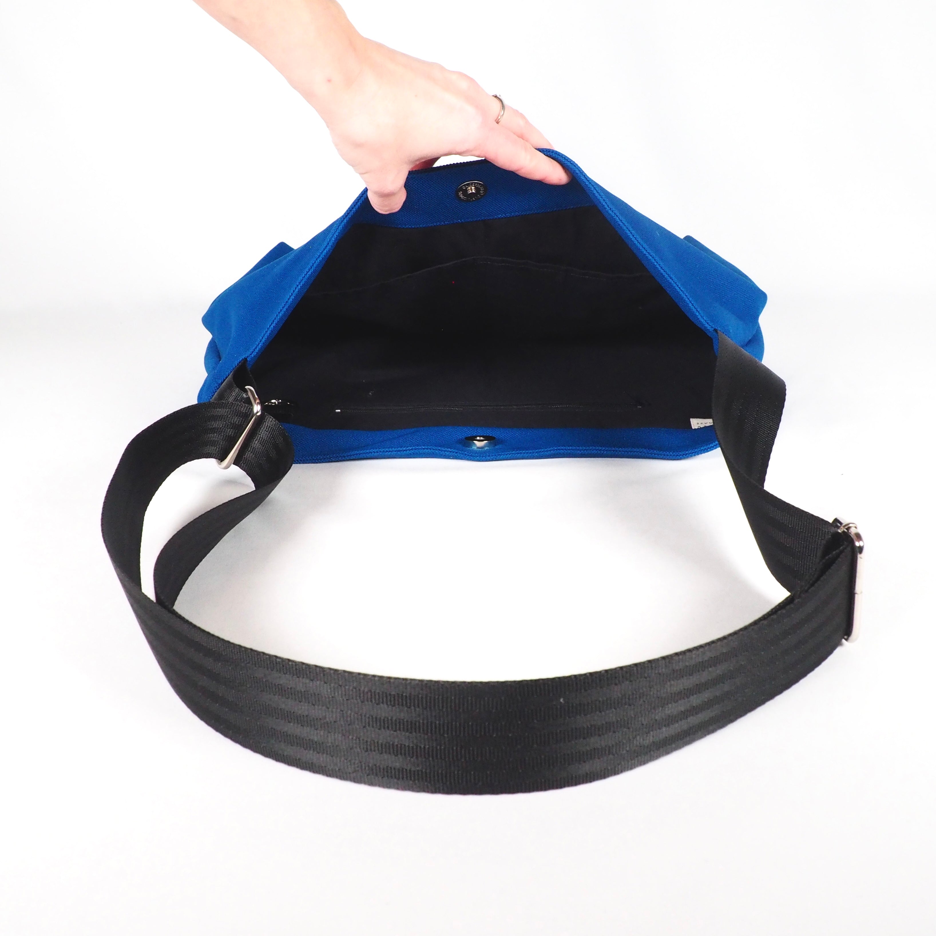 Eine geöffnete blaue Umhängetasche mit schwarzem Riemen wird von einer Hand gehalten.