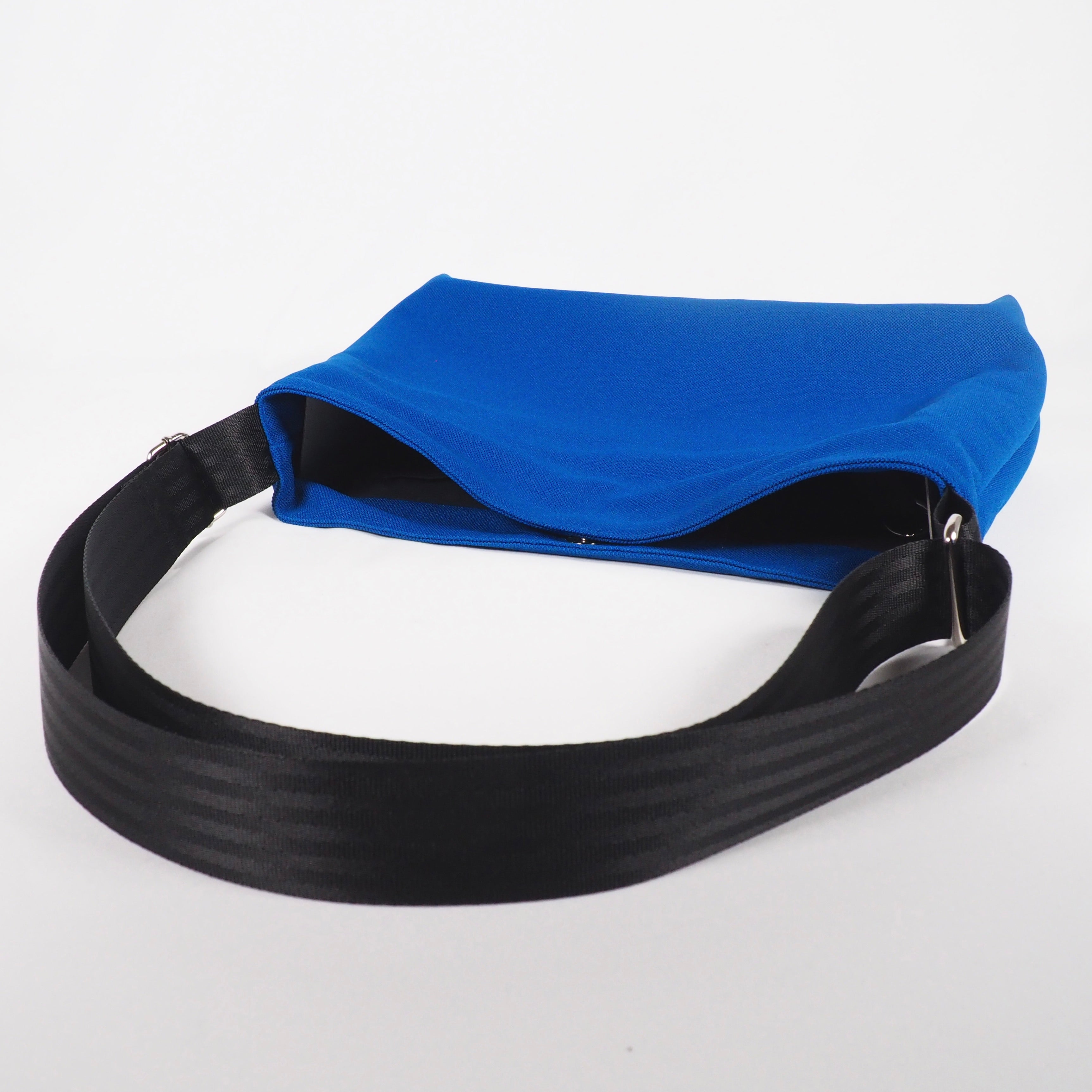 Blaue Tasche mit schwarzem Schultergurt, liegend auf einer weißen Oberfläche.