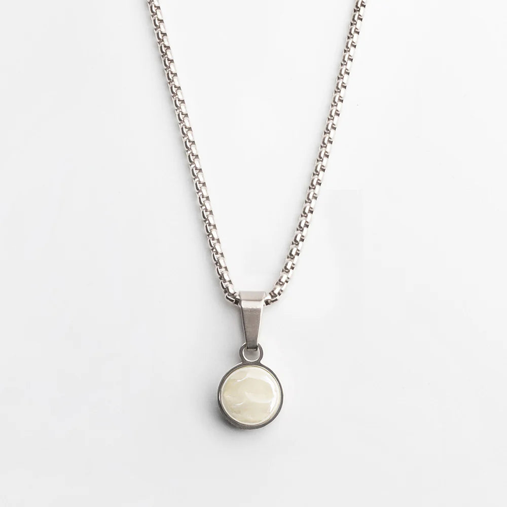 Eine silberne Kette mit einem runden Anhänger mit einem cremeweißen, glänzenden Stein, der in eine Metallfassung gefasst ist, auf weißem Hintergrund.
