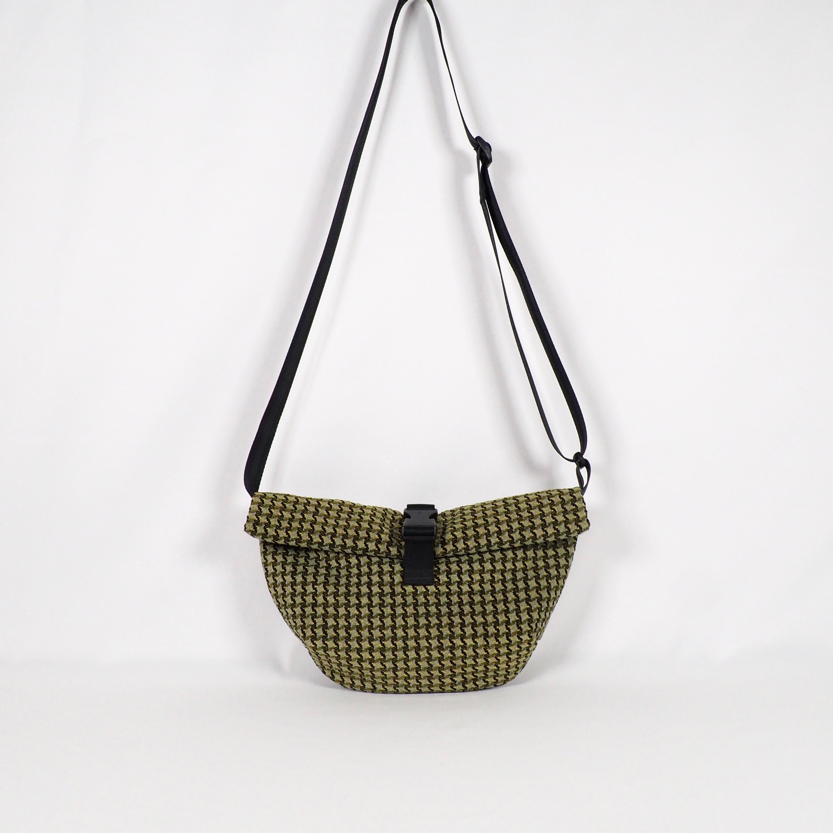 Schultertasche mit schwarz-weißem Hahnentrittmuster und schwarzem Riemen vor weißem Hintergrund.