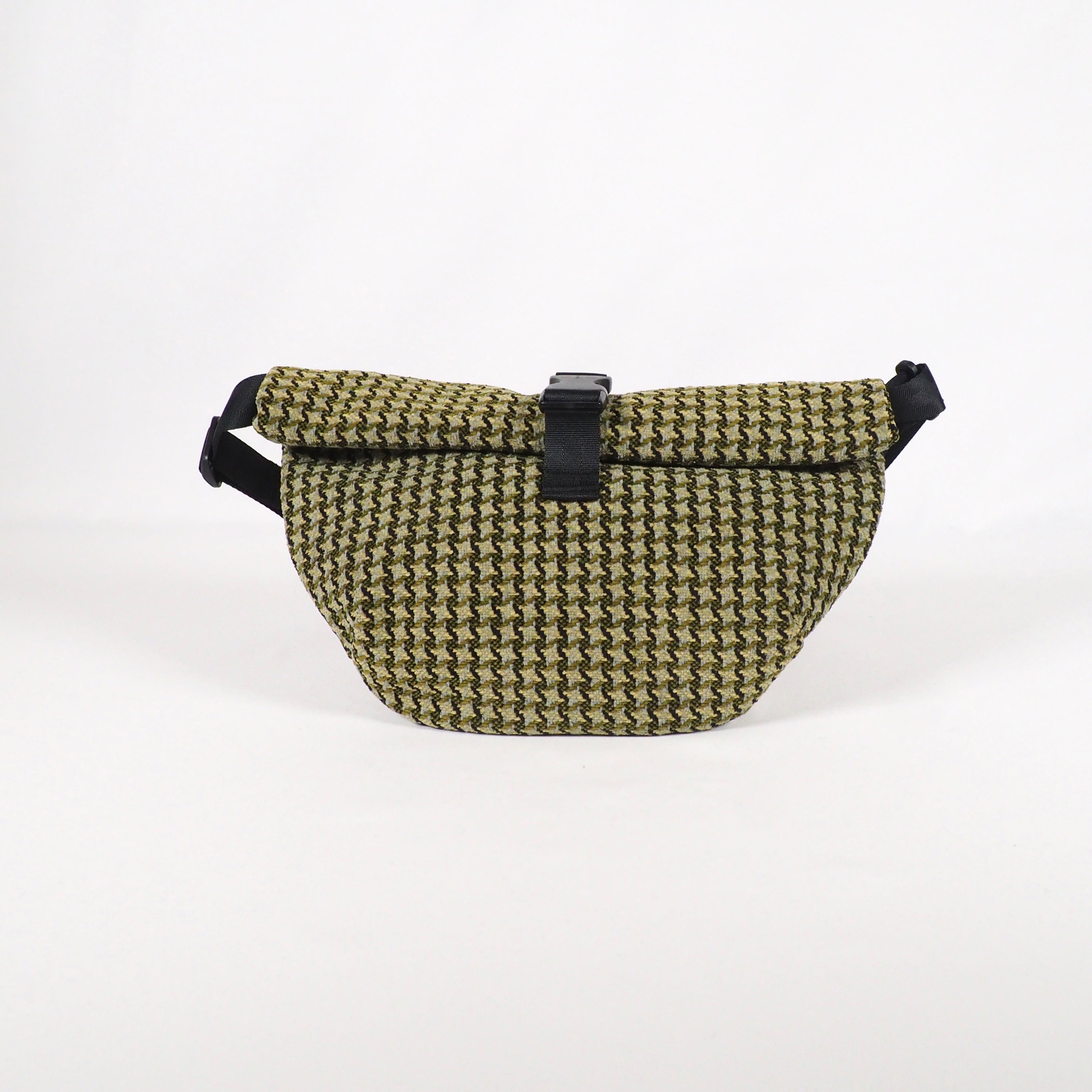 Grüne Umhängetasche mit einem Rautenmuster und einem schwarzen Verschlussband auf weißem Hintergrund.