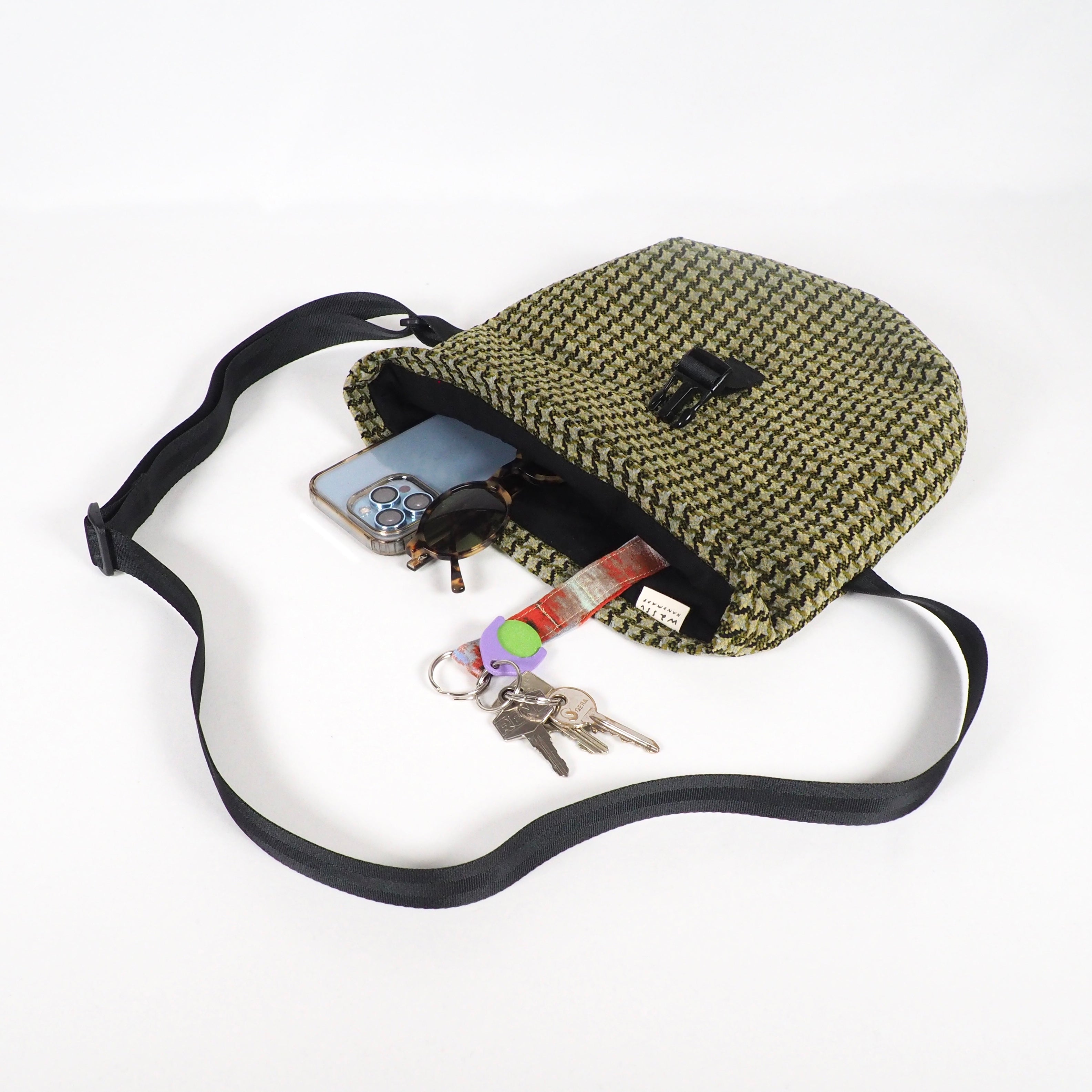 Eine geöffnete Tasche mit Handy, Sonnenbrille, Schlüsseln und anderen Kleinigkeiten auf einem weißen Hintergrund.