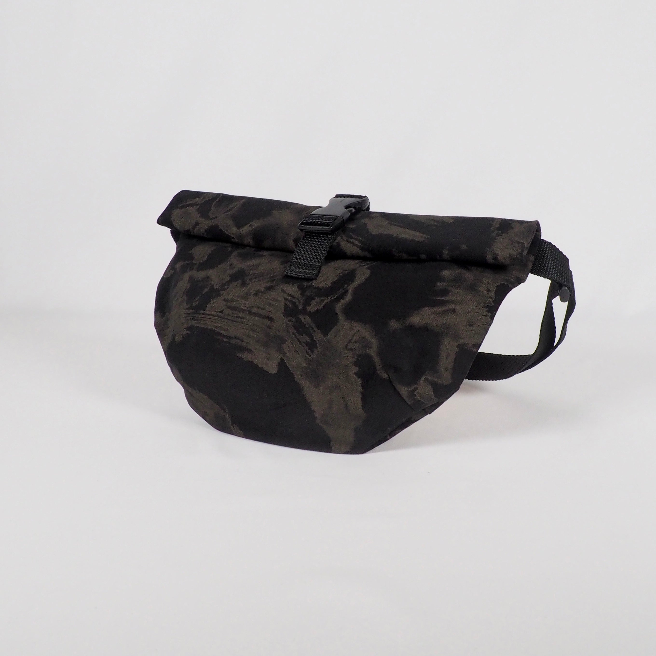 Schwarze Gürteltasche mit Rollenverschluss und Tarnmuster, auf weißem Hintergrund.