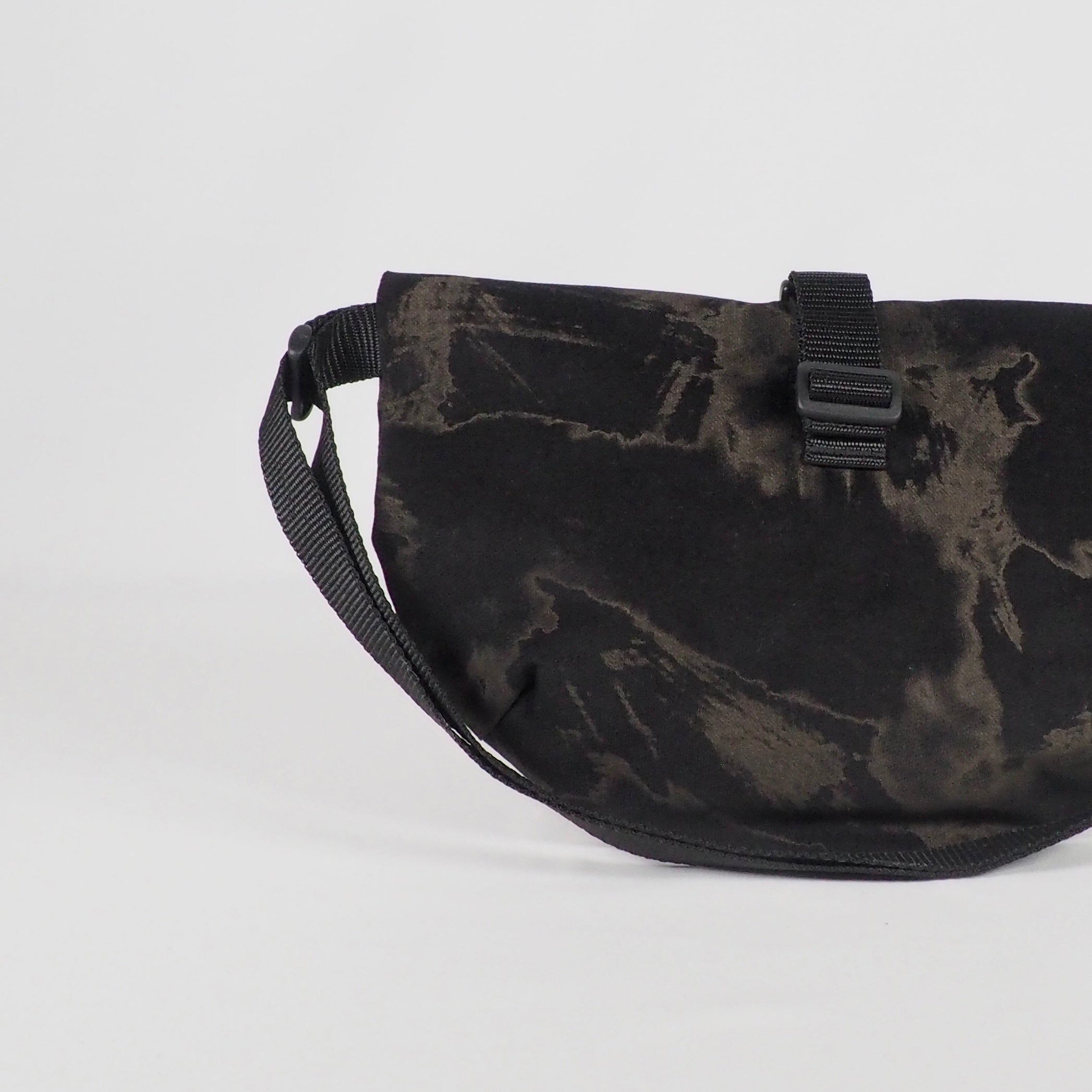 Schwarze Umhängetasche mit einem abstrakten Muster und Schnalle auf weißem Hintergrund dargestellt.