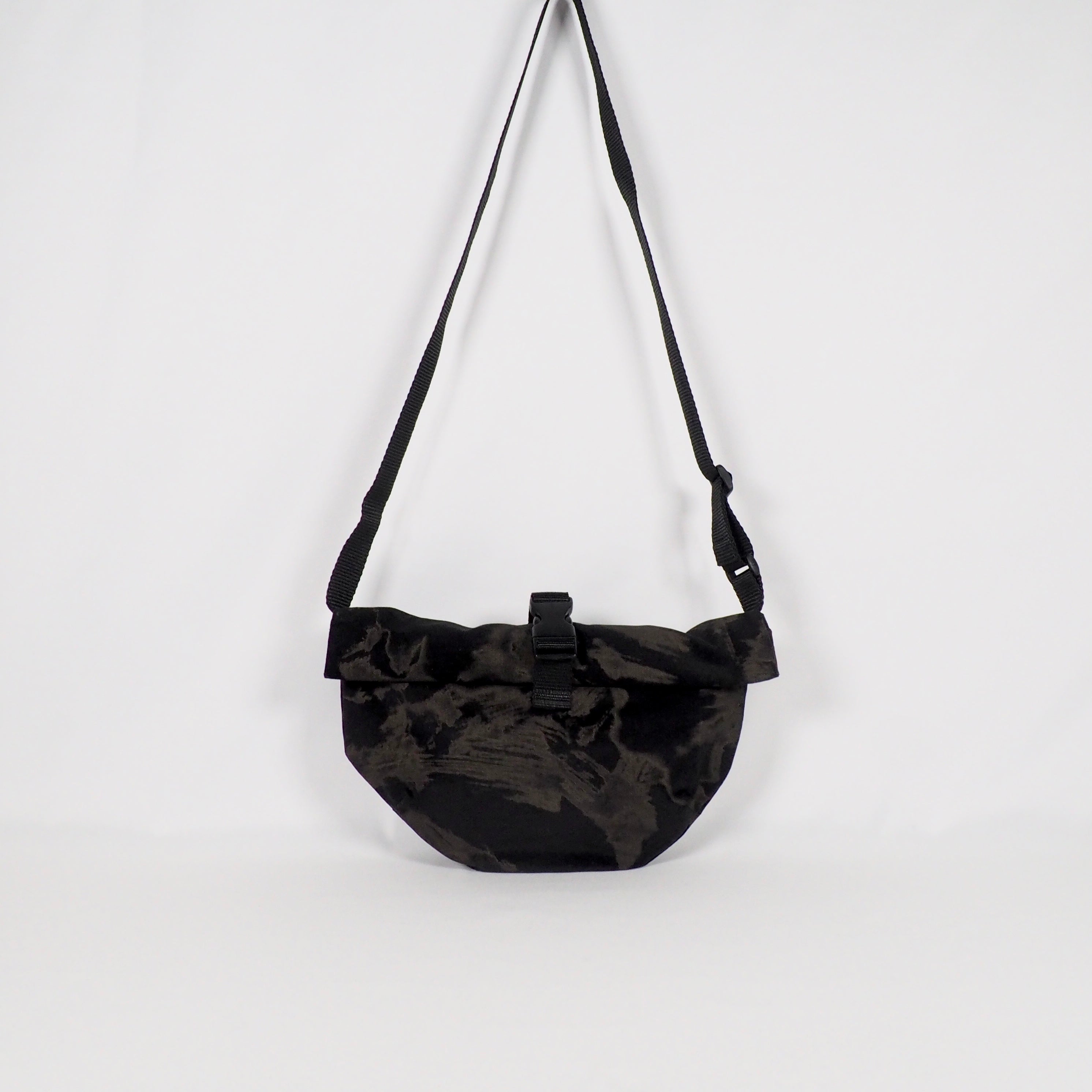 Schwarze Umhängetasche mit Schnalle, die an einem weißen Hintergrund hängt.