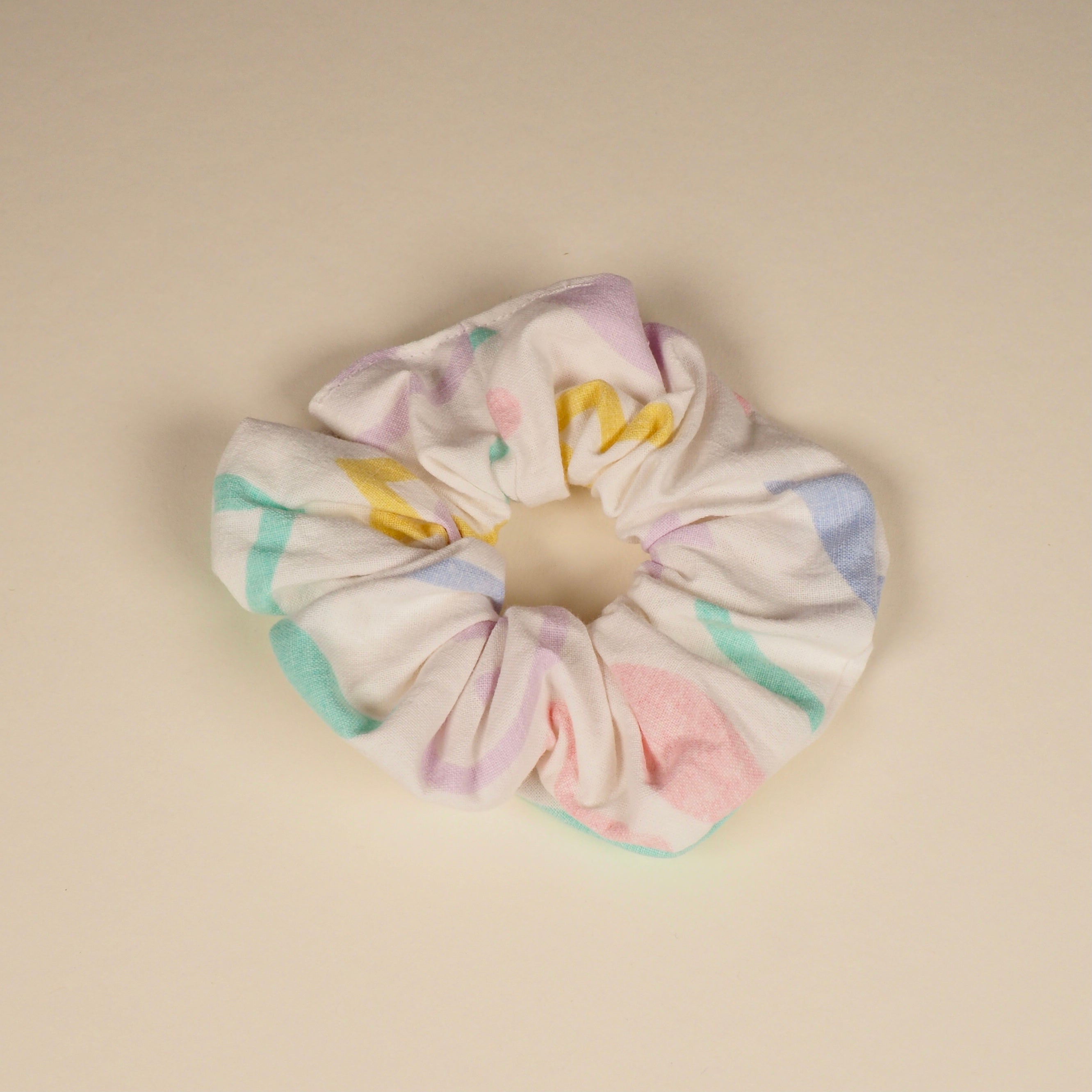 Ein pastellfarbiges Haargummi mit abstrakten Mustern liegt auf einem hellen Hintergrund.