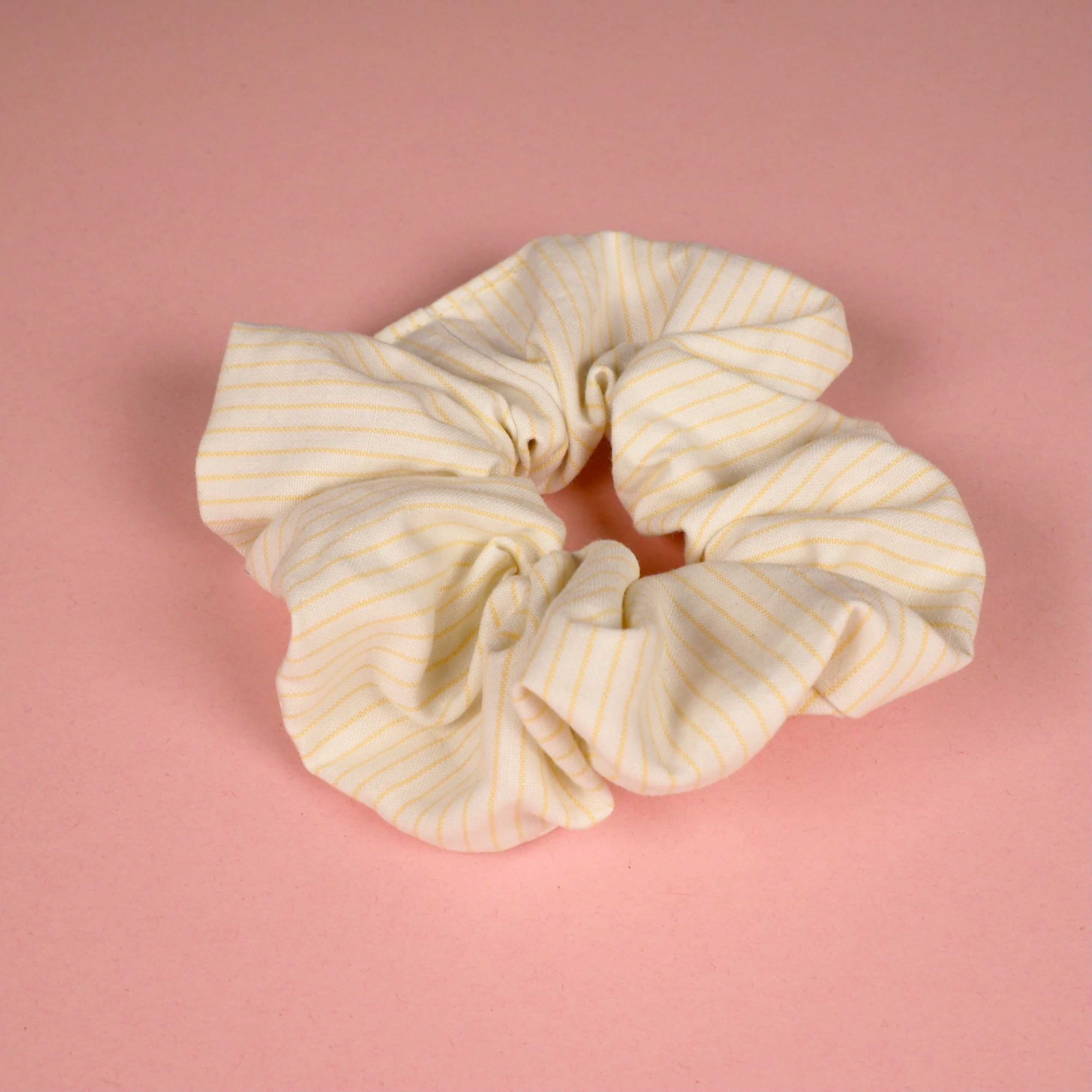 Beiger Scrunchie mit gelben Streifen auf rosa Hintergrund.