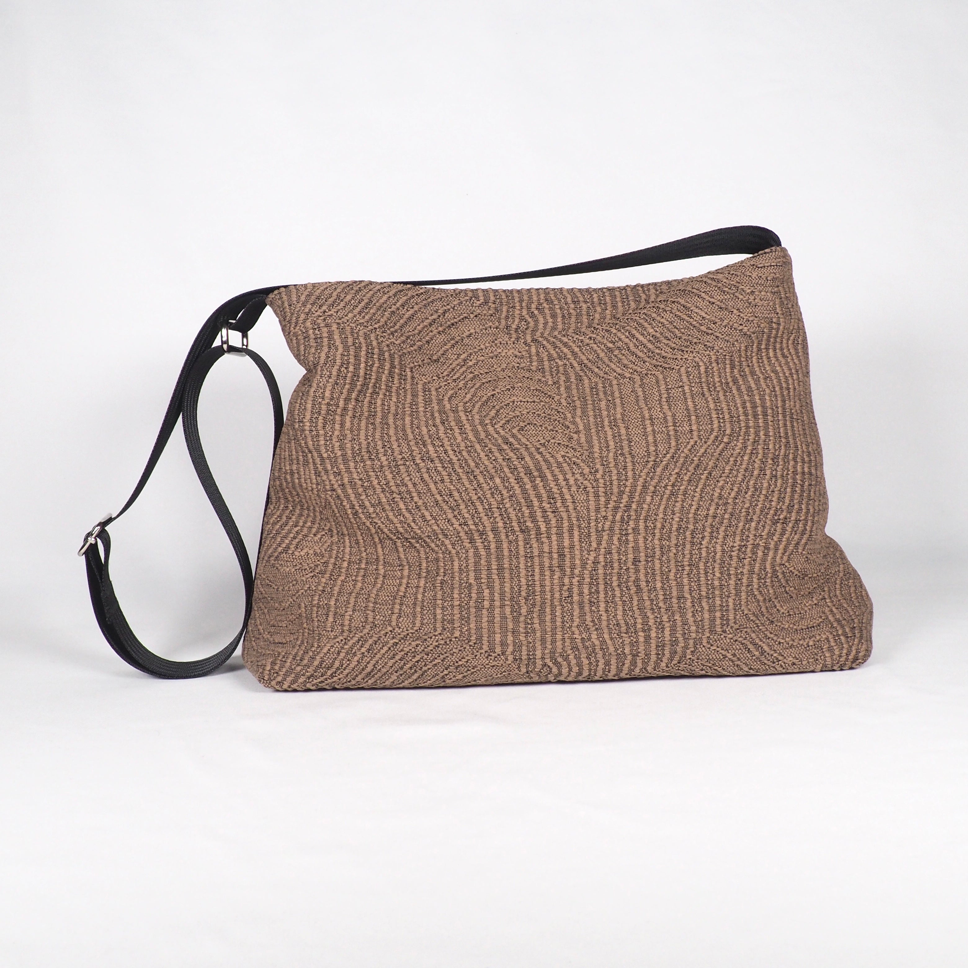 Braune Stofftasche mit schwarzem Schulterriemen, auf weißem Hintergrund.