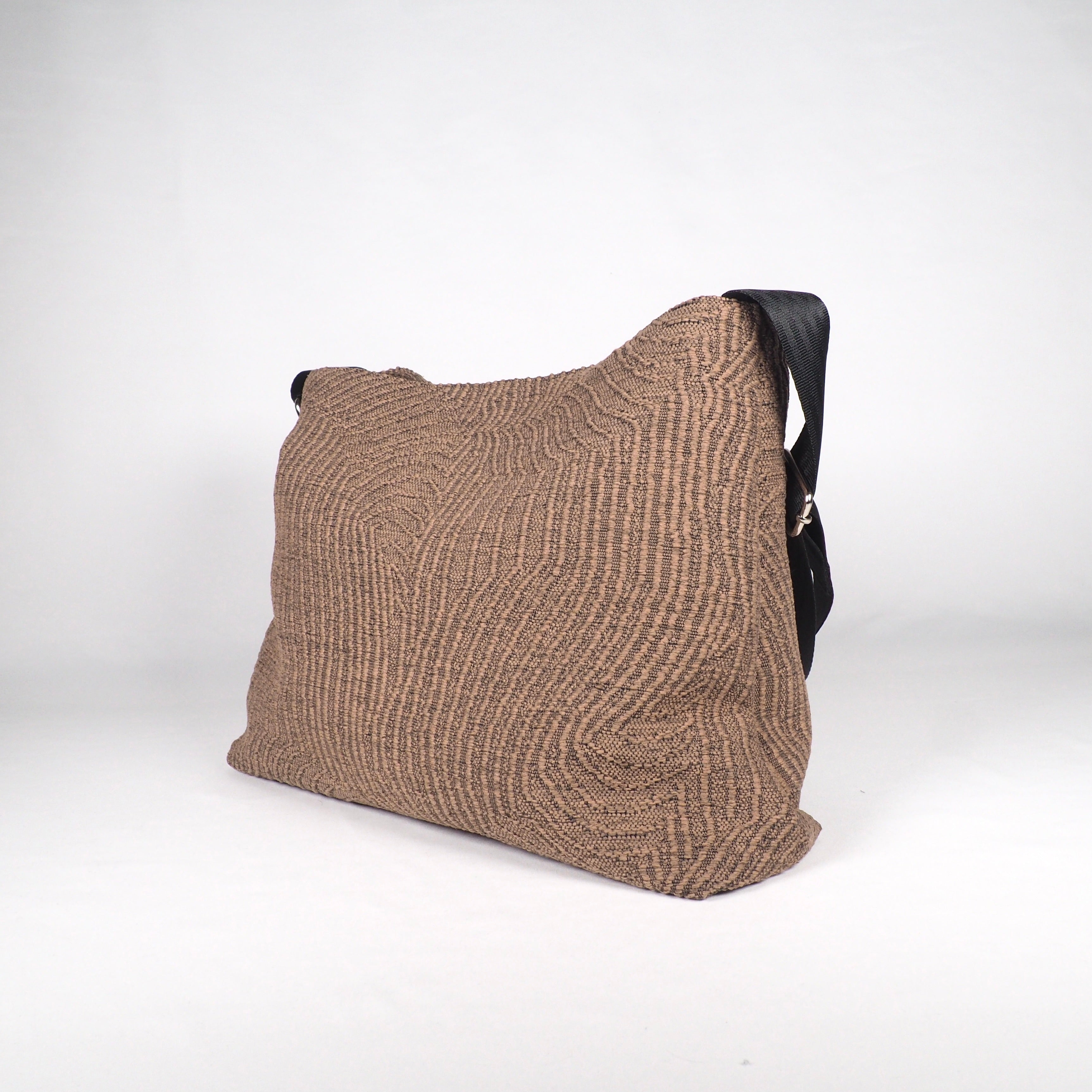 Beige Tasche mit gewelltem Muster und schwarzem Schultergurt, auf einem hellen Hintergrund fotografiert.