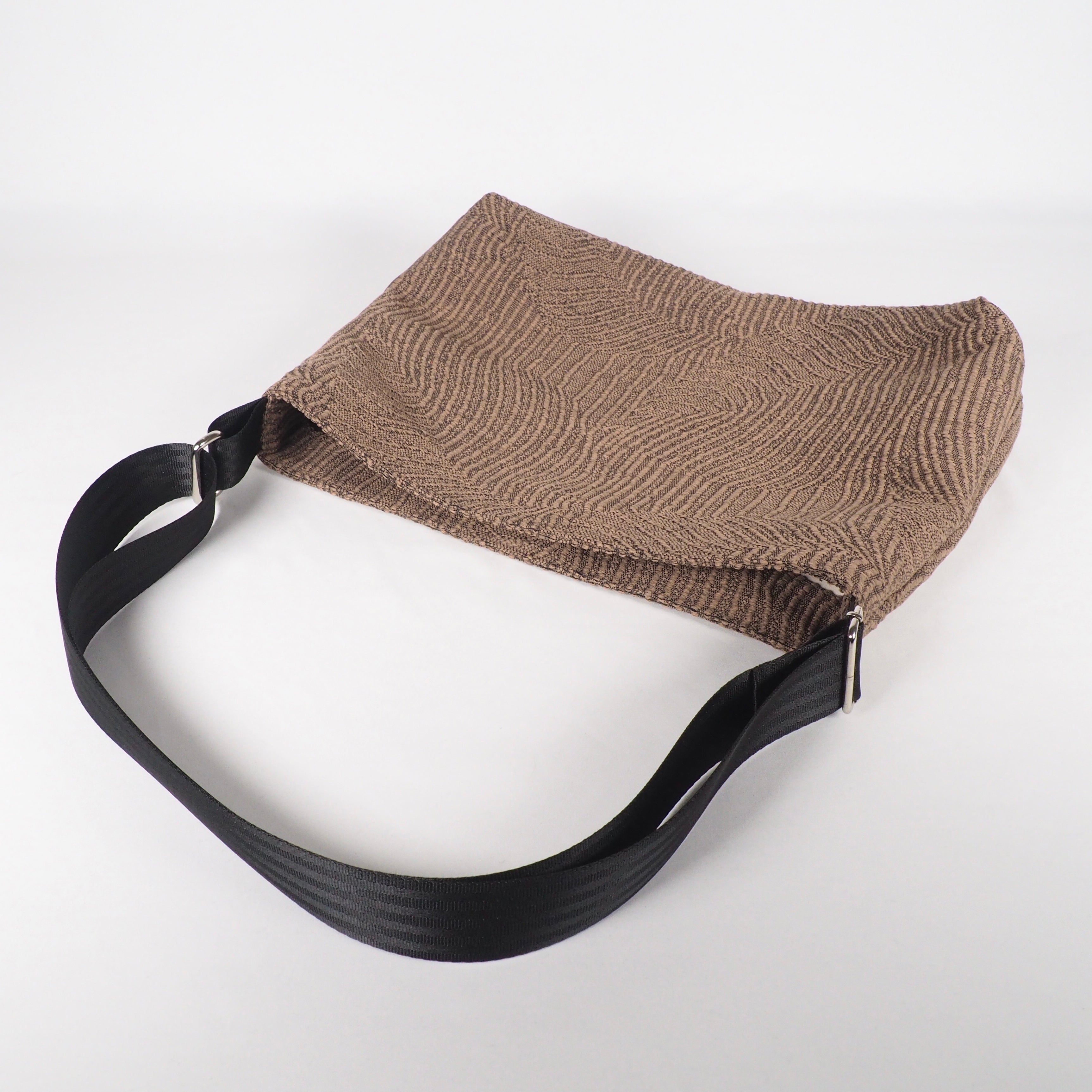 Braune Tasche mit strukturiertem Muster und schwarzem Schulterriemen vor einem weißen Hintergrund.